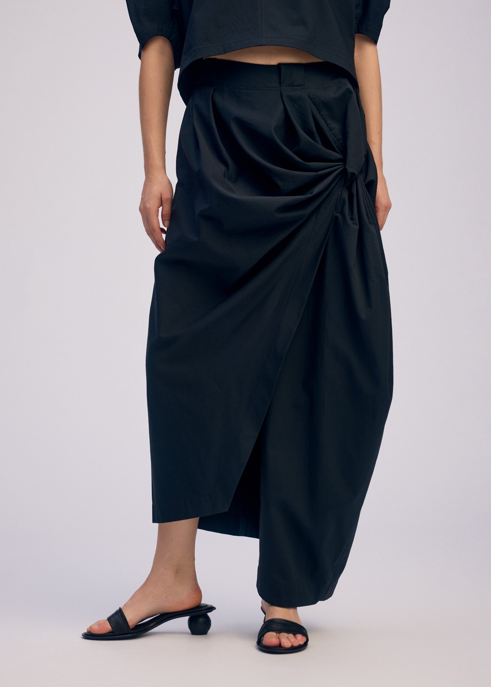 A model wears the ISSEY MIYAKE TWISTED DRAPE trousers.