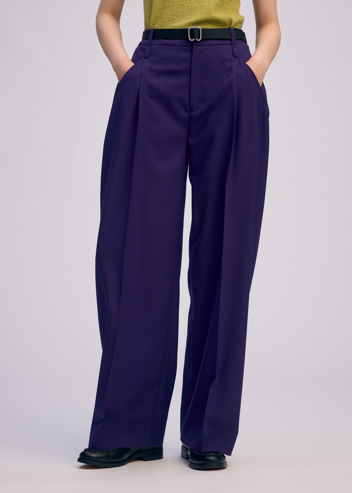 A model wears the ISSEY MIYAKE BELTED WOOL PANTS trousers.