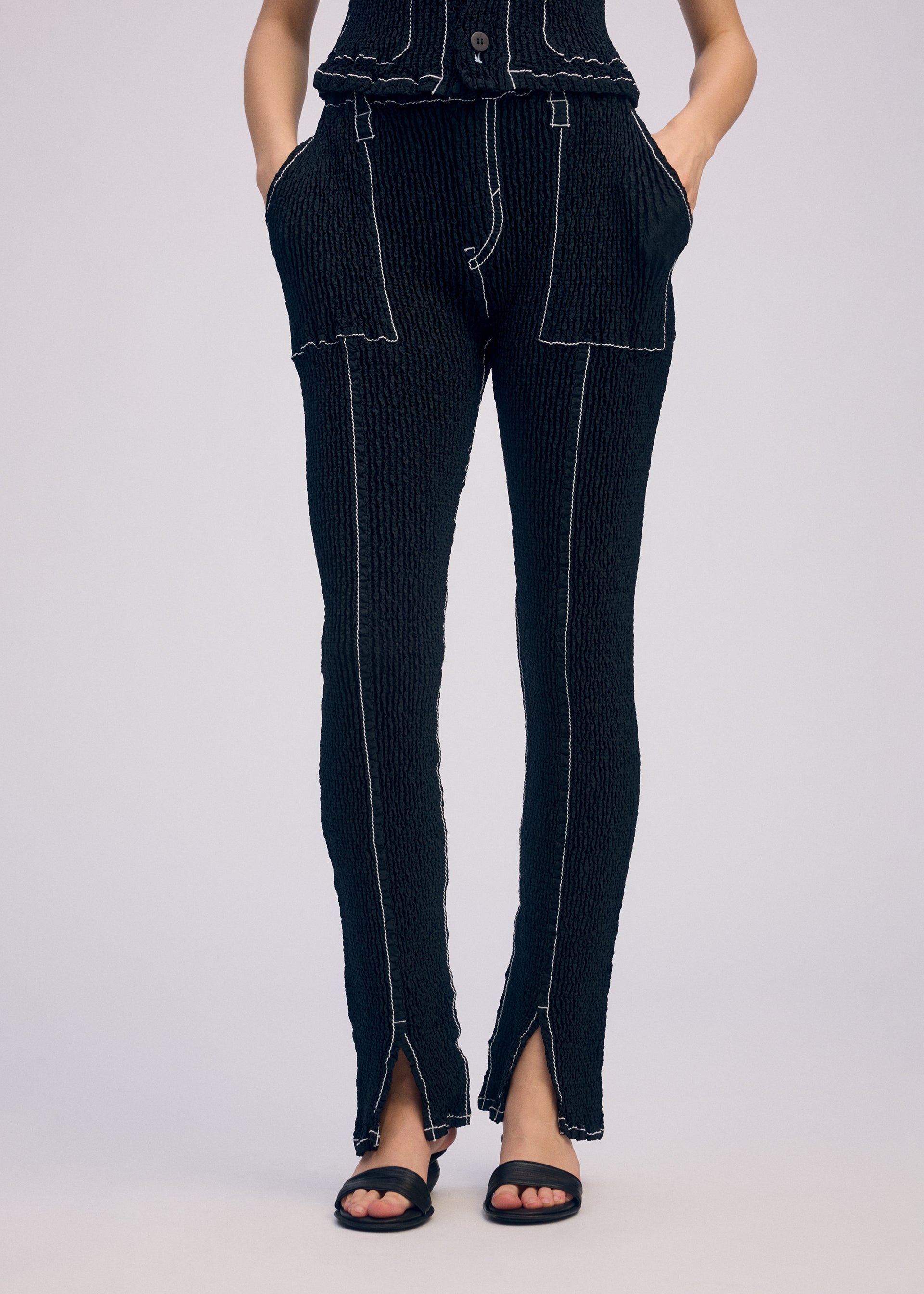 A model wears the ISSEY MIYAKE WAVELET ENSEMBLE trousers.