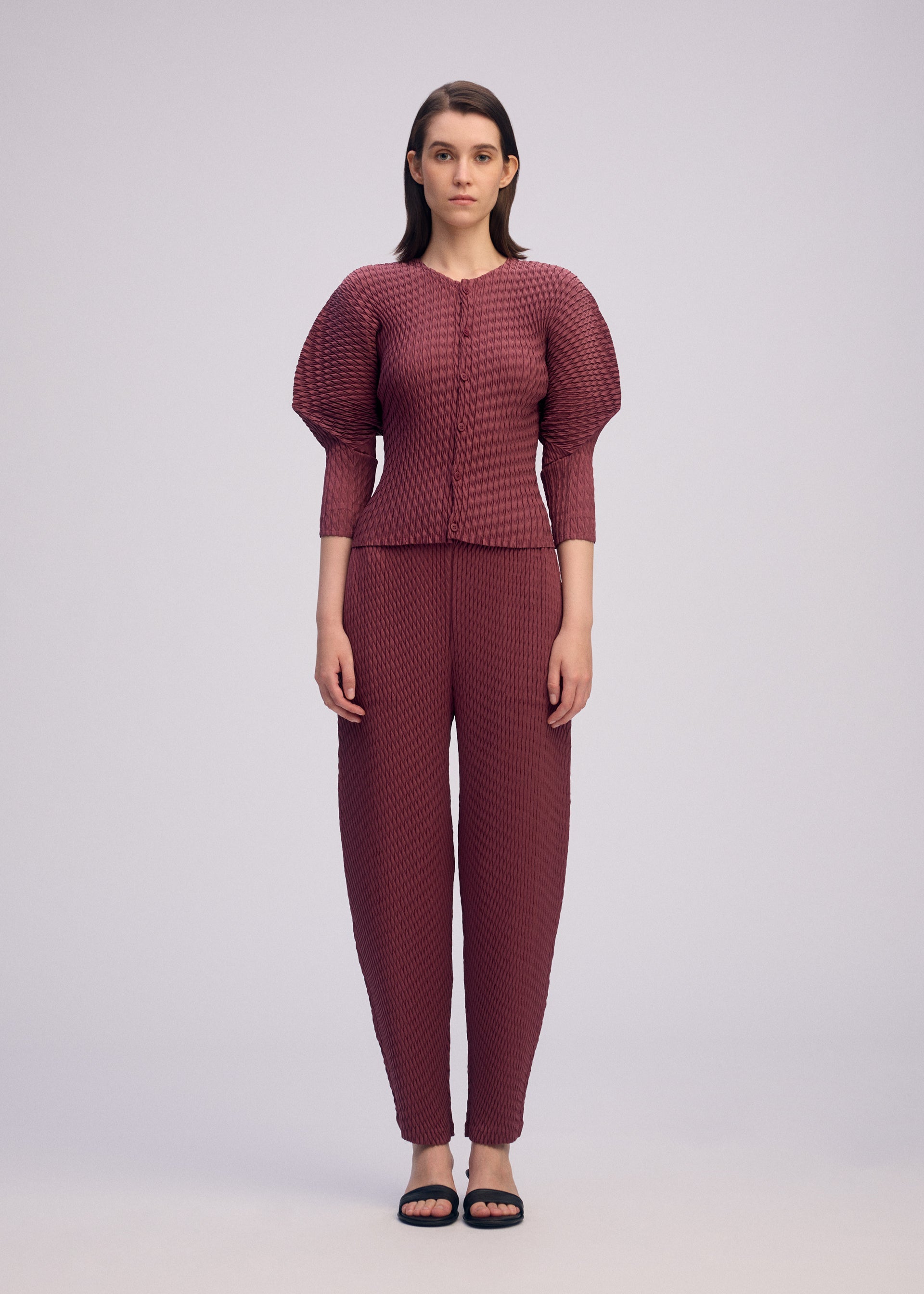 A model wears the ISSEY MIYAKE SLEEK PLEATS sleek-pleats-trousers-burgundy.