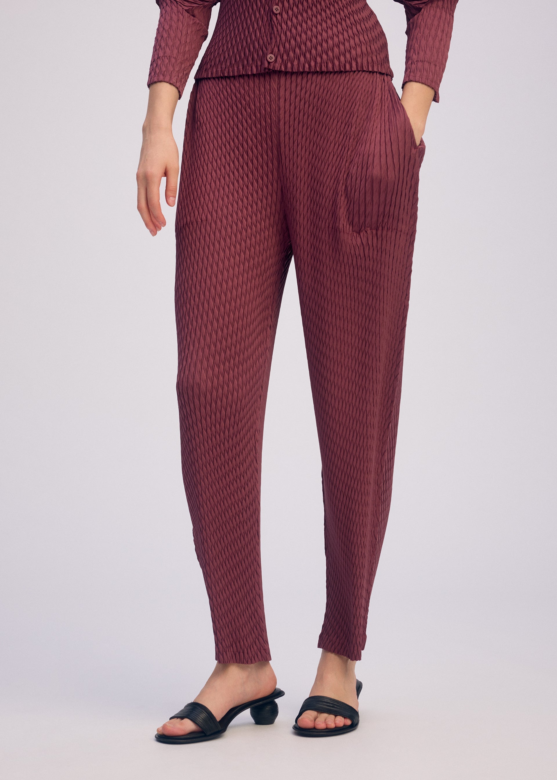 A model wears the ISSEY MIYAKE SLEEK PLEATS sleek-pleats-trousers-light-grey-1.