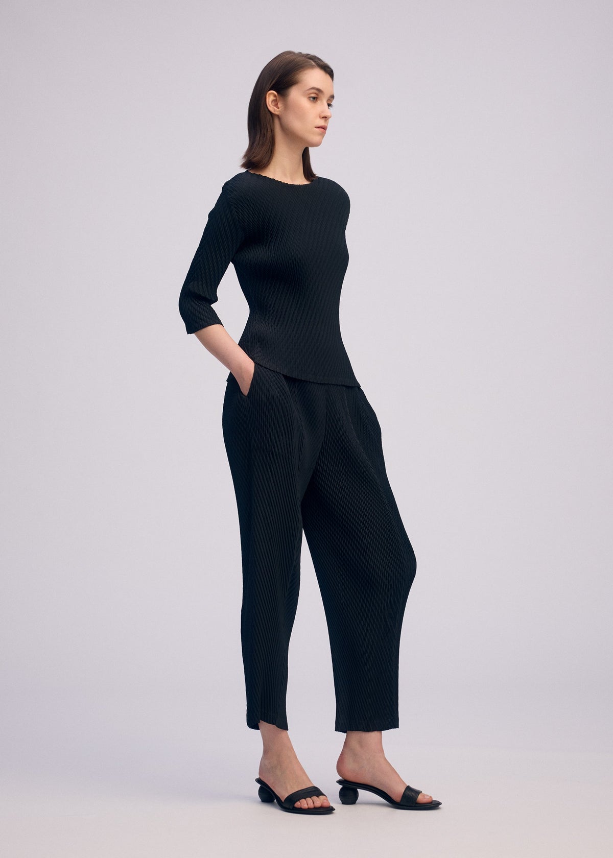 A model wears the ISSEY MIYAKE RHOMBUS PLEATS trousers.