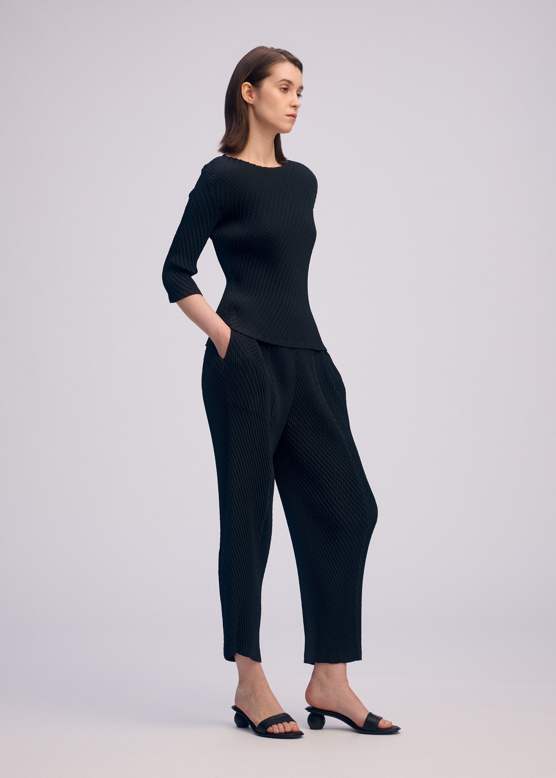A model wears the ISSEY MIYAKE RHOMBUS PLEATS trousers.