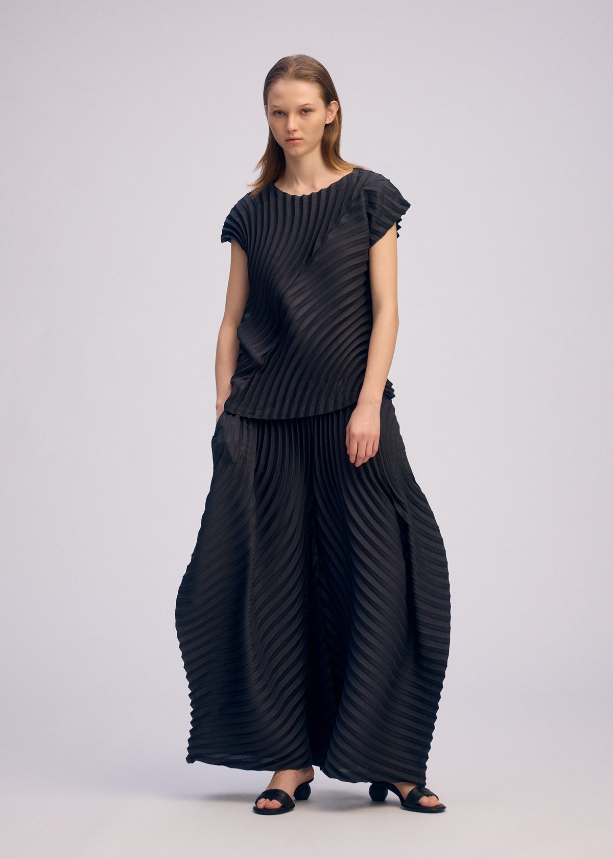 A model wears the ISSEY MIYAKE CIRCLE PLEATS PB trousers.