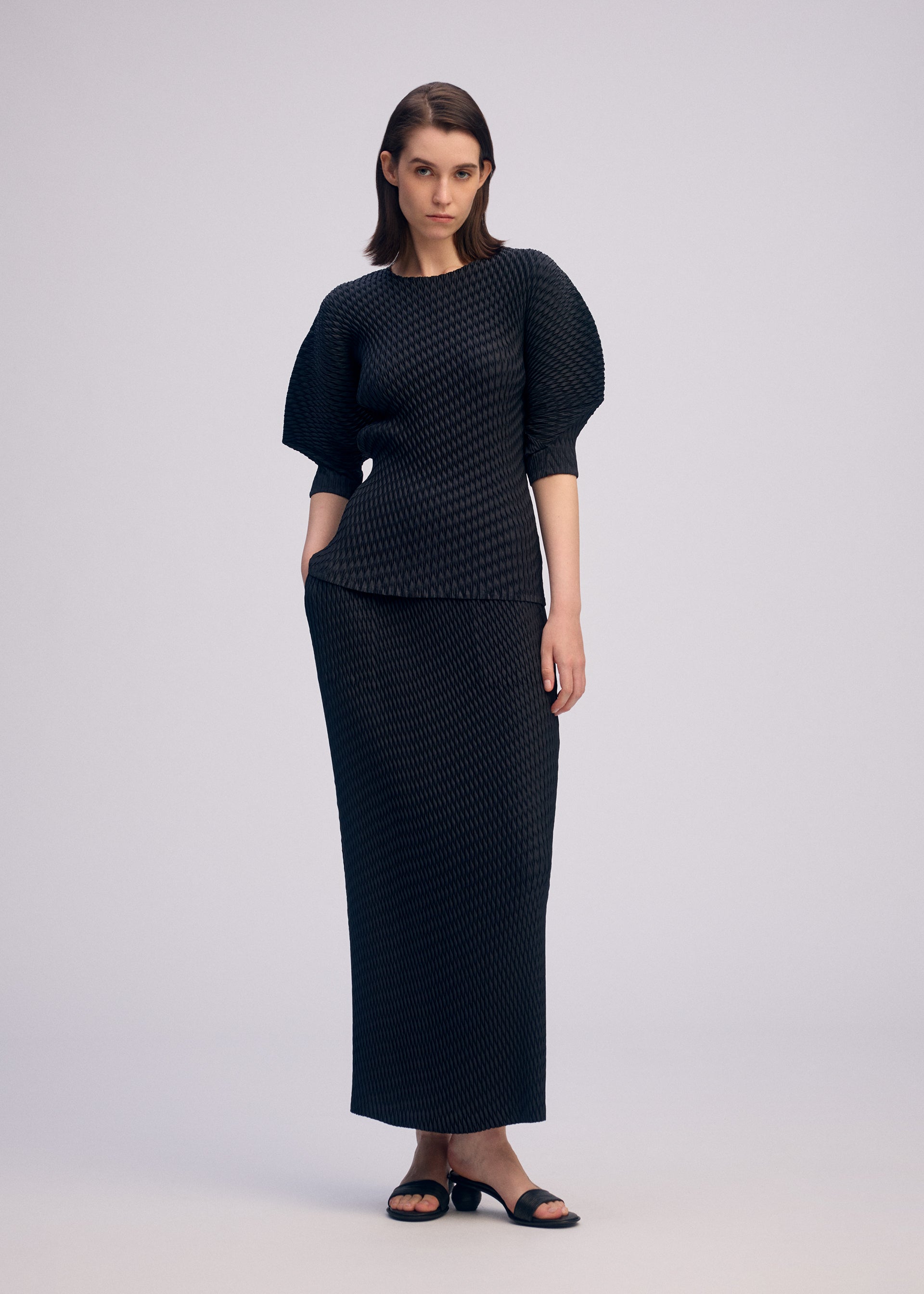 A model wears the ISSEY MIYAKE SLEEK PLEATS sleek-pleats-skirt-burgundy.