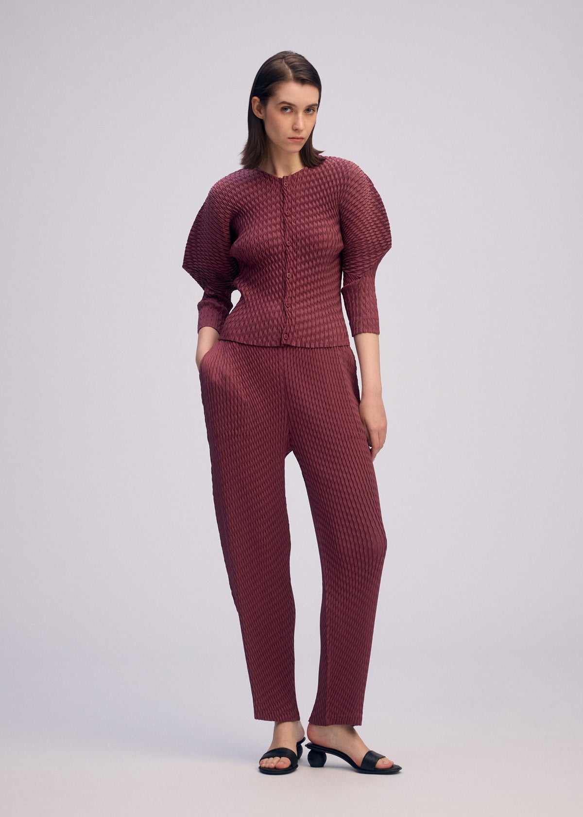 A model wears the ISSEY MIYAKE SLEEK PLEATS sleek-pleats-cardigan-light-grey.