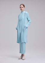 A model wears the ISSEY MIYAKE HATCHING PLEATS hatching-pleats-three-quarter-length-coat-black.