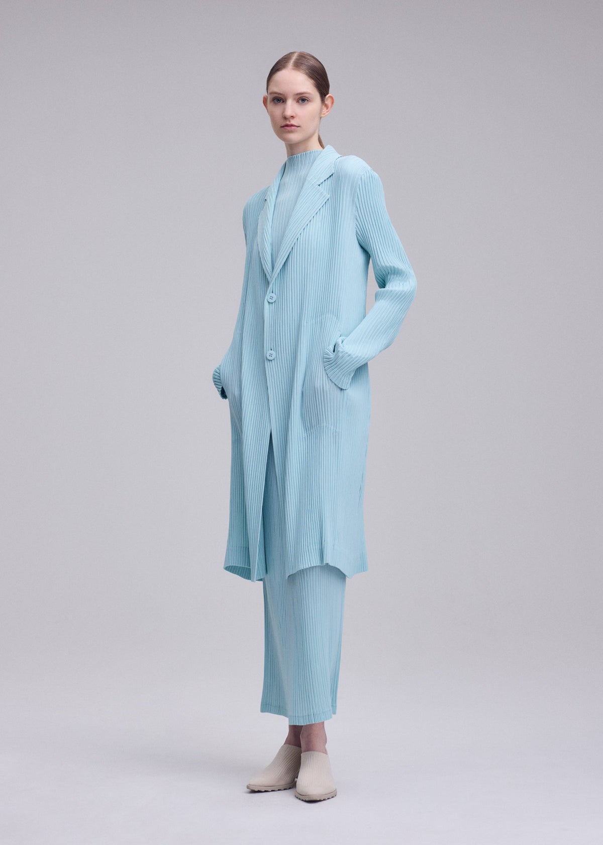 A model wears the ISSEY MIYAKE HATCHING PLEATS hatching-pleats-three-quarter-length-coat-black.