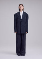 A model wears the ISSEY MIYAKE HONEST ENSEMBLE honest-ensemble-blazer-jacket-black.