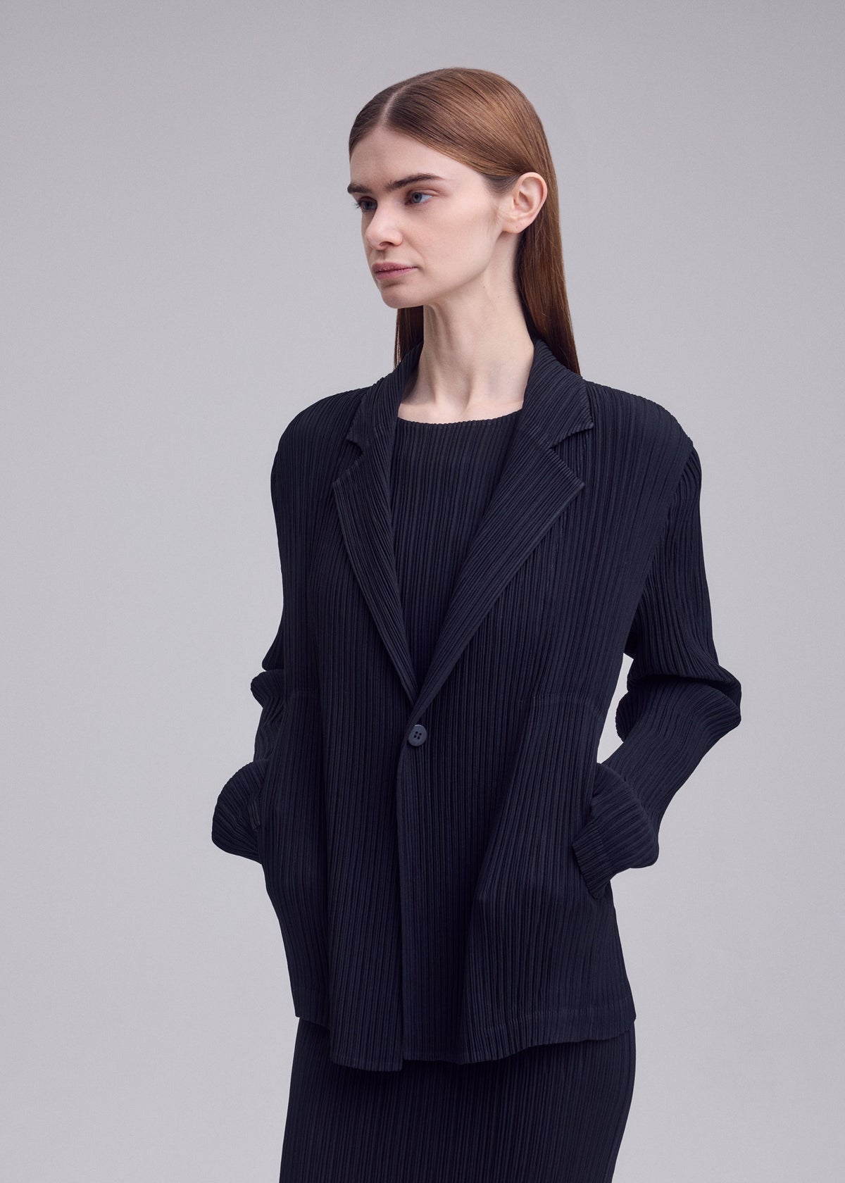A model wears the ISSEY MIYAKE HATCHING PLEATS hatching-pleats-blazer-style-jacket-grey.