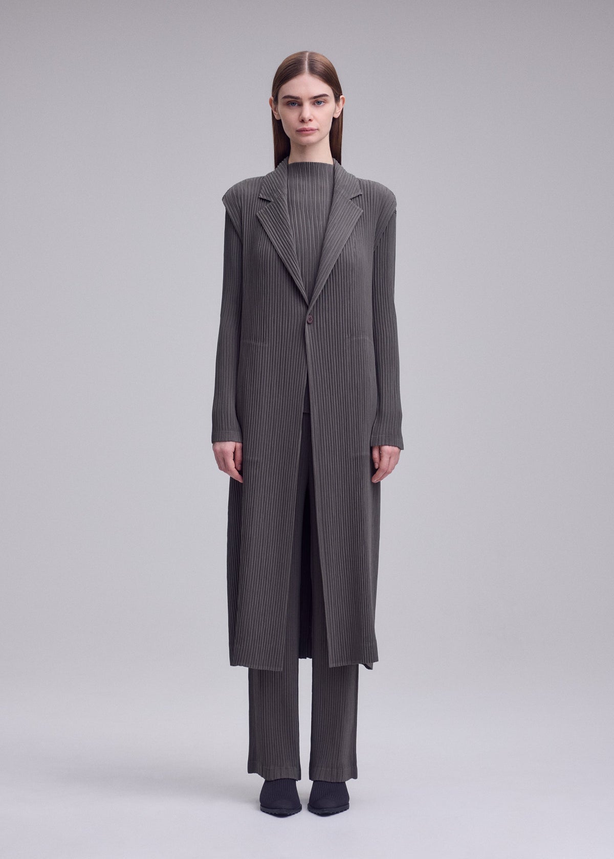 A model wears the ISSEY MIYAKE HATCHING PLEATS hatching-pleats-mid-length-vest-grey.