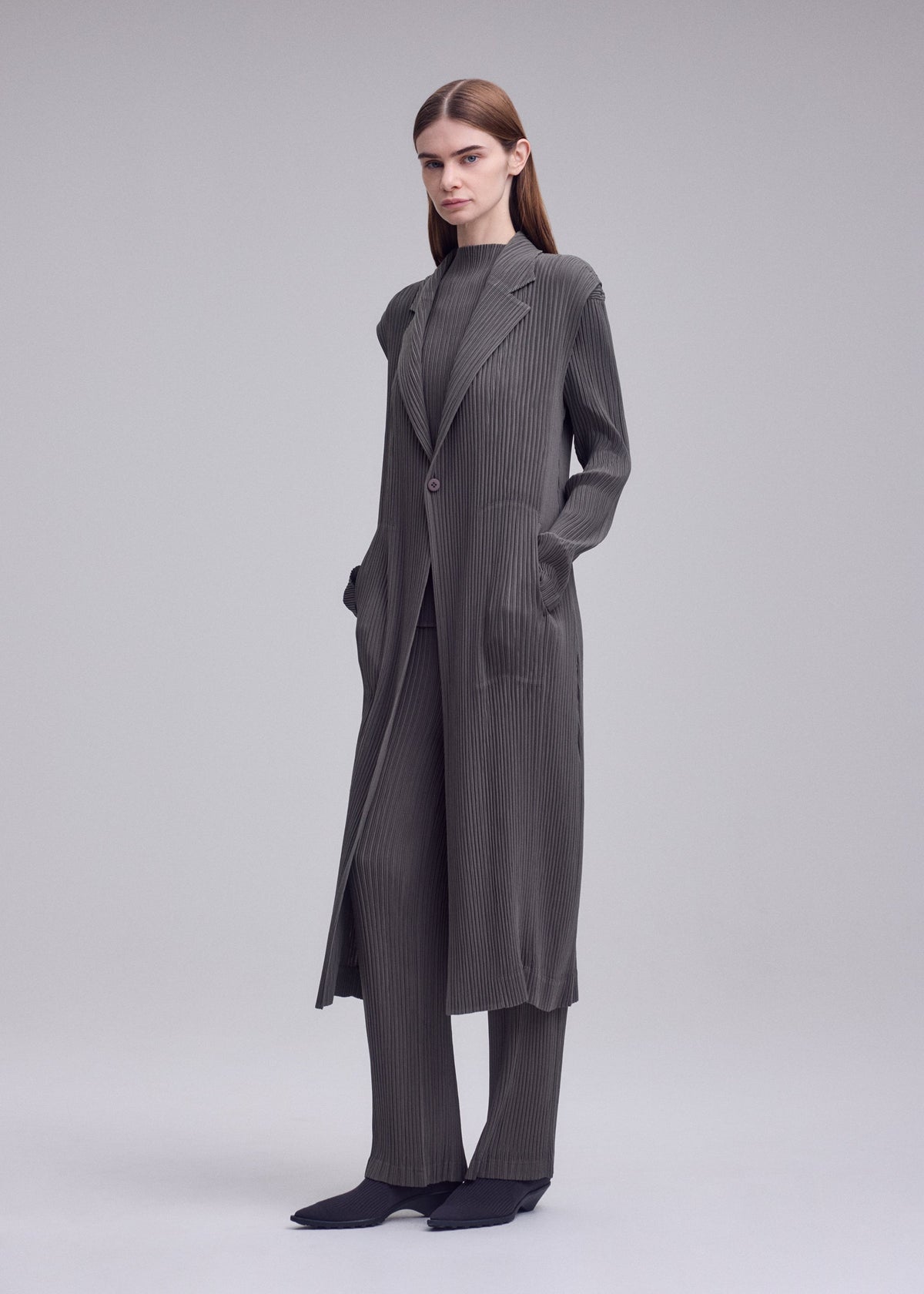A model wears the ISSEY MIYAKE HATCHING PLEATS hatching-pleats-mid-length-vest-black.