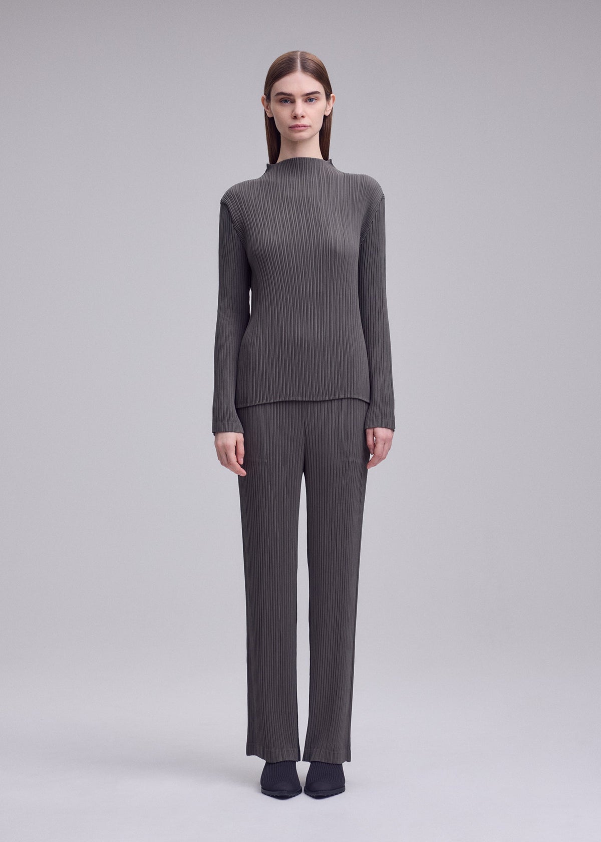 A model wears the ISSEY MIYAKE HATCHING PLEATS hatching-pleats-classic-cut-trousers-black.