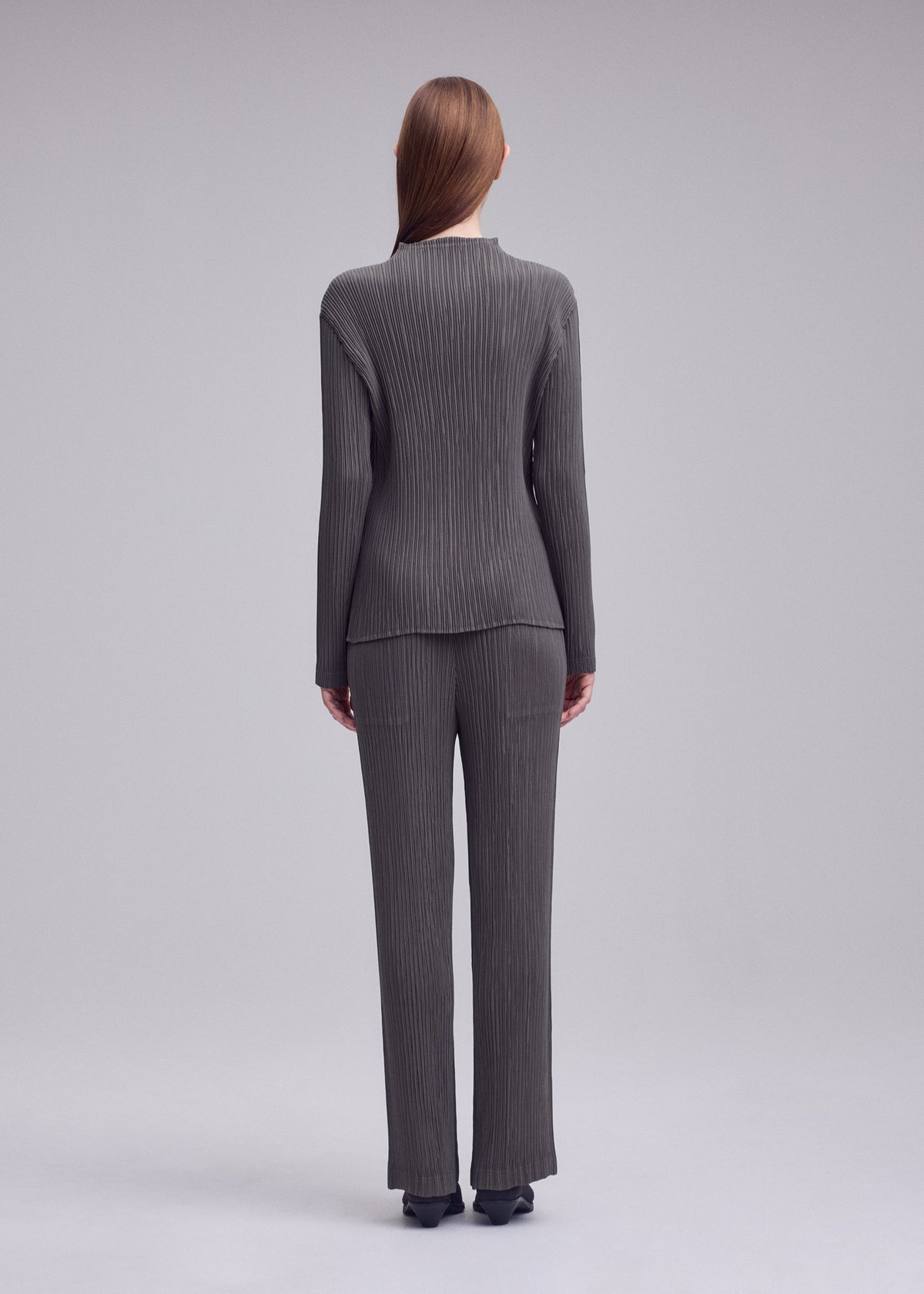 A model wears the ISSEY MIYAKE HATCHING PLEATS hatching-pleats-classic-cut-trousers-black.