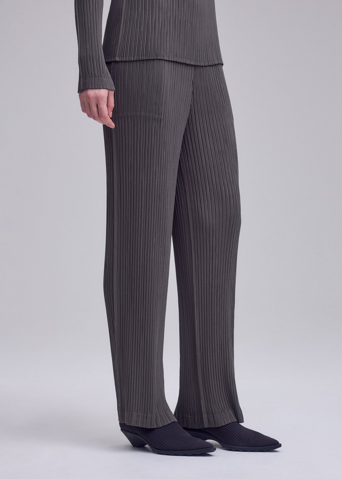 A model wears the ISSEY MIYAKE HATCHING PLEATS hatching-pleats-classic-cut-trousers-grey.