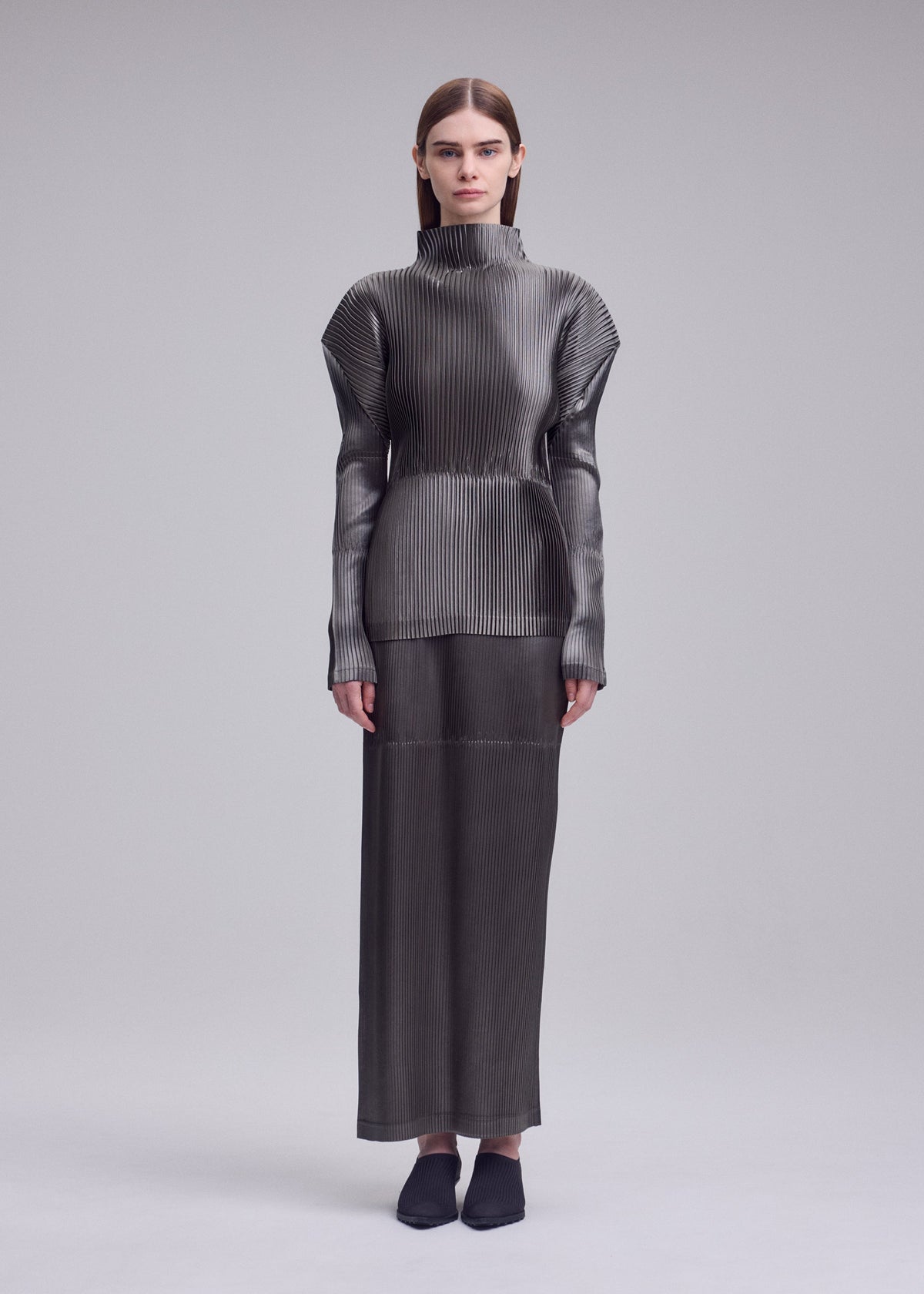 A model wears the ISSEY MIYAKE GLOSSED PANELS PLEATS glossed-panels-pleats-skirt-grey.