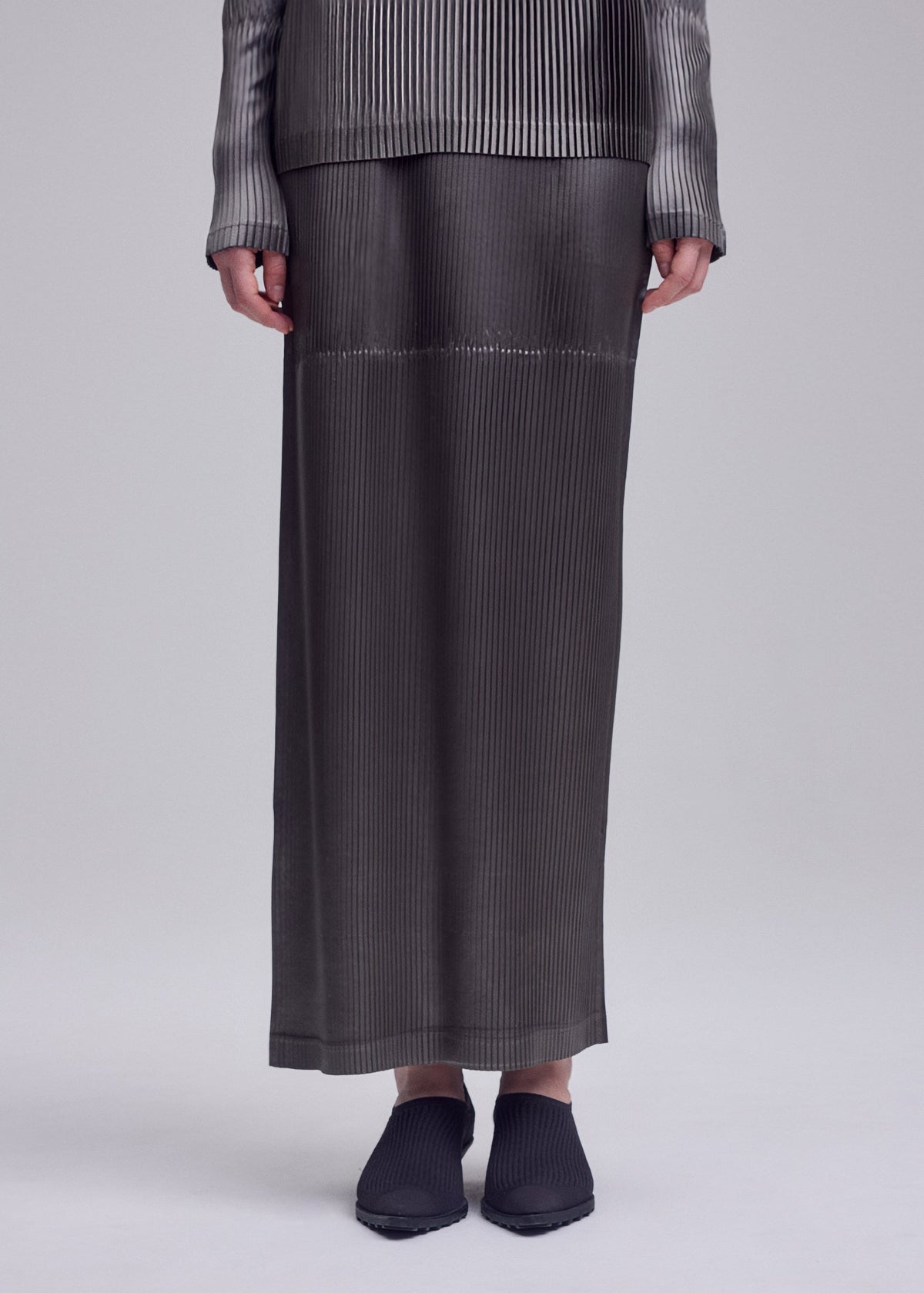 A model wears the ISSEY MIYAKE GLOSSED PANELS PLEATS glossed-panels-pleats-skirt-light-pink.