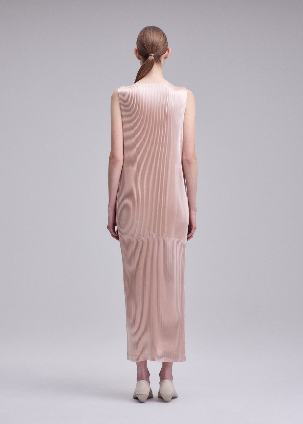 A model wears the ISSEY MIYAKE GLOSSED PANELS PLEATS glossed-panels-pleats-dress-light-pink.