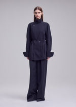 A model wears the ISSEY MIYAKE MONSIEUR SHIRT monsieur-shirt-bolo-tie-belt-shirt-white.