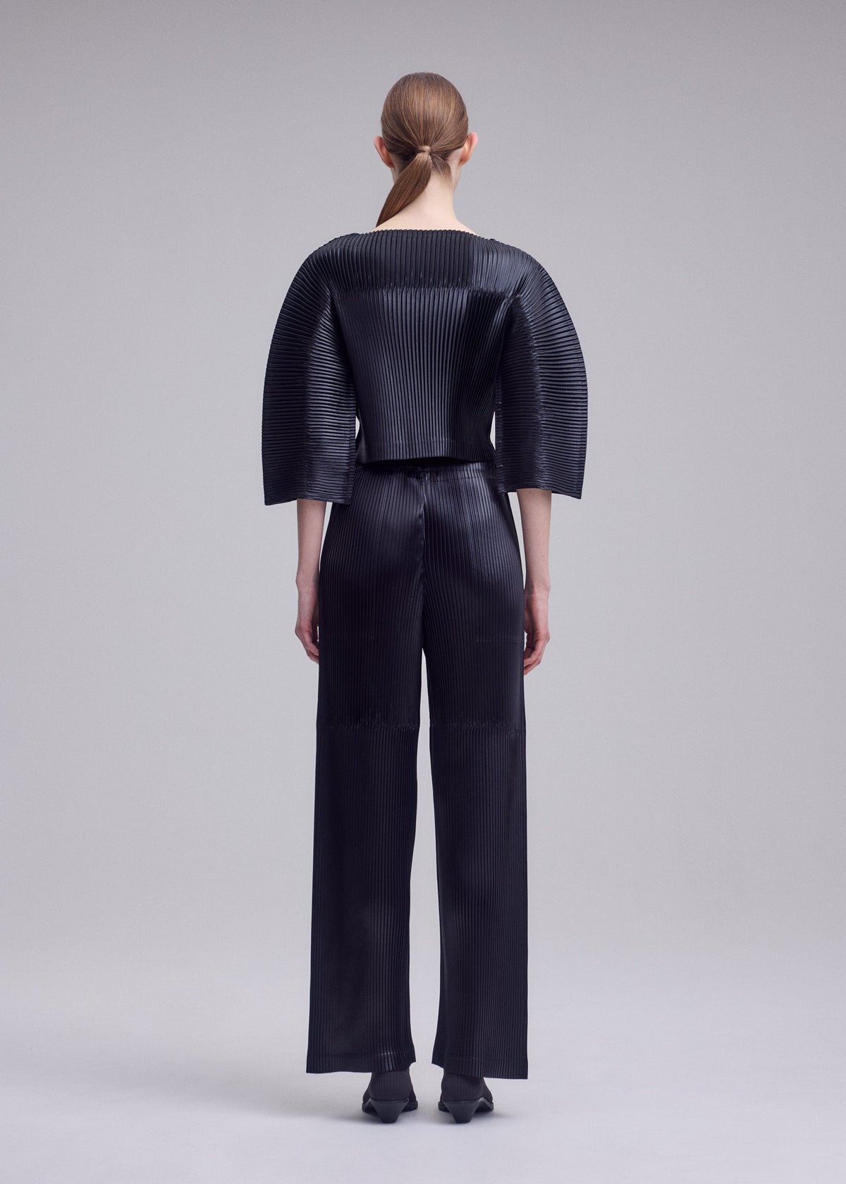 A model wears the ISSEY MIYAKE GLOSSED PANELS PLEATS glossed-panels-pleats-cropped-top-light-pink.