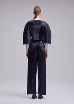 A model wears the ISSEY MIYAKE GLOSSED PANELS PLEATS glossed-panels-pleats-cropped-top-black.