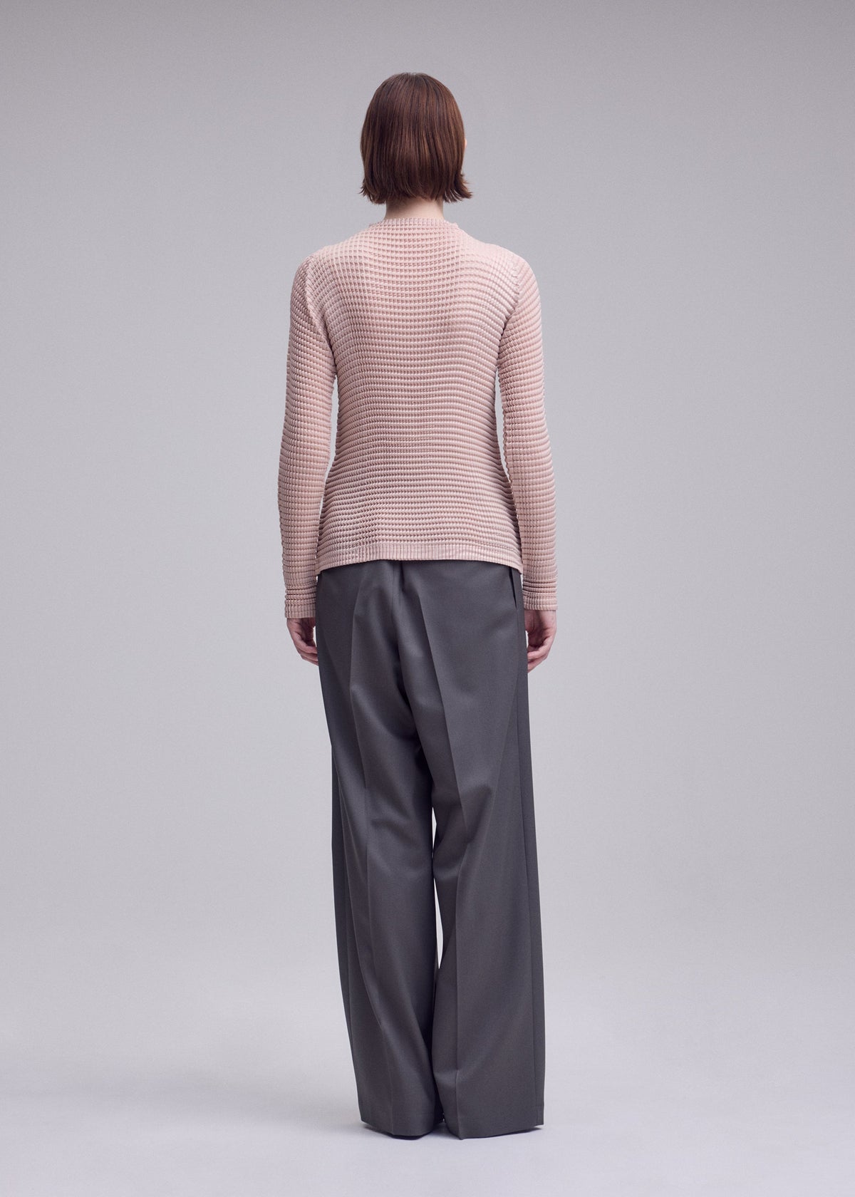 A model wears the ISSEY MIYAKE SUEDE LIKE PLEATS suede-like-pleats-long-sleeved-top-light-pink.