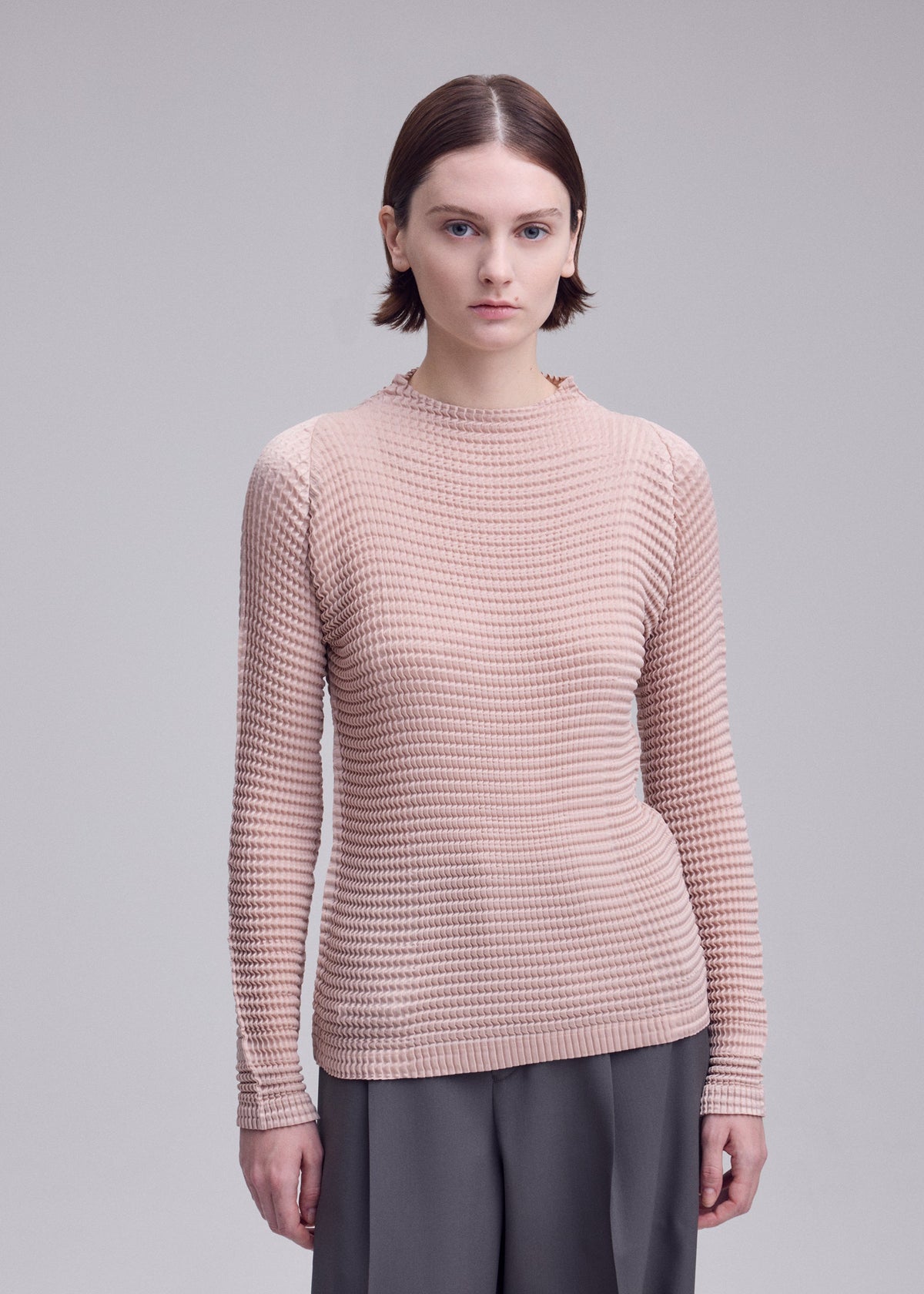 A model wears the ISSEY MIYAKE SUEDE LIKE PLEATS suede-like-pleats-long-sleeved-top-light-pink.