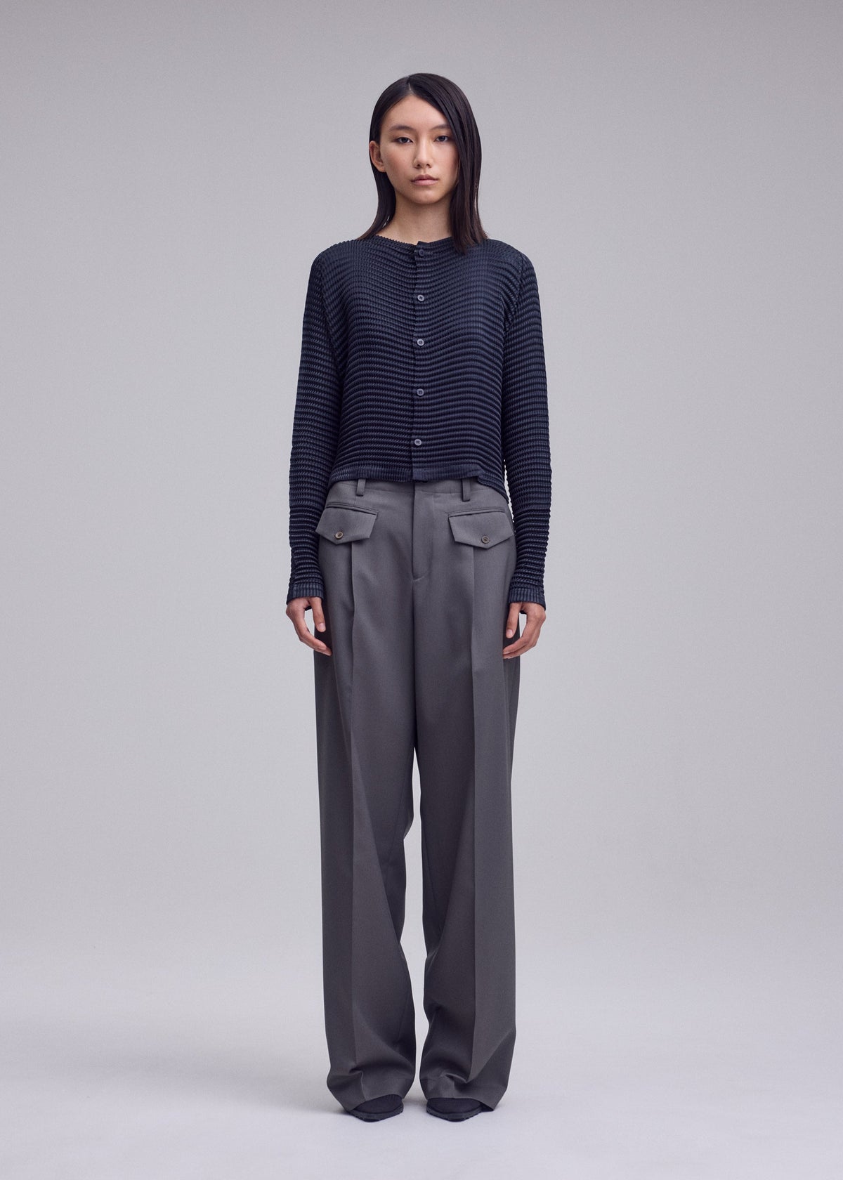 A model wears the ISSEY MIYAKE SUEDE LIKE PLEATS suede-like-pleats-round-neck-cardigan-grey.