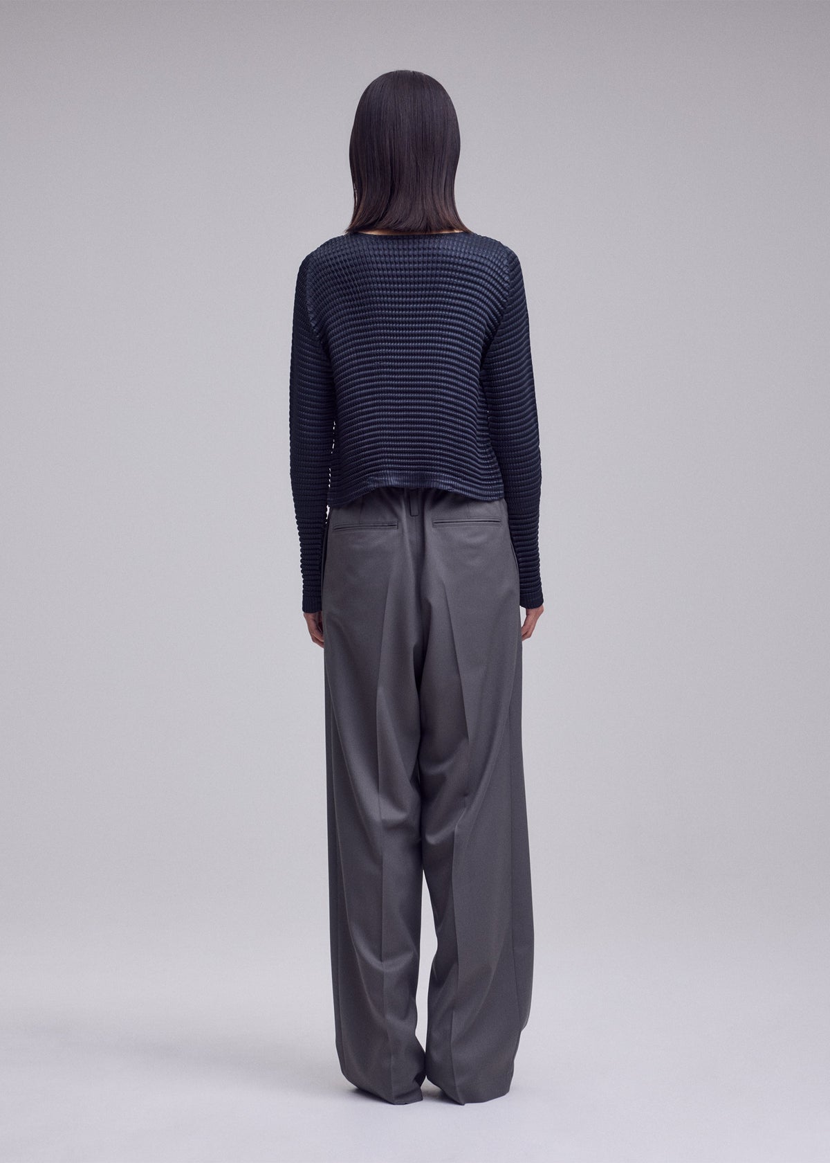 A model wears the ISSEY MIYAKE SUEDE LIKE PLEATS suede-like-pleats-round-neck-cardigan-light-pink.