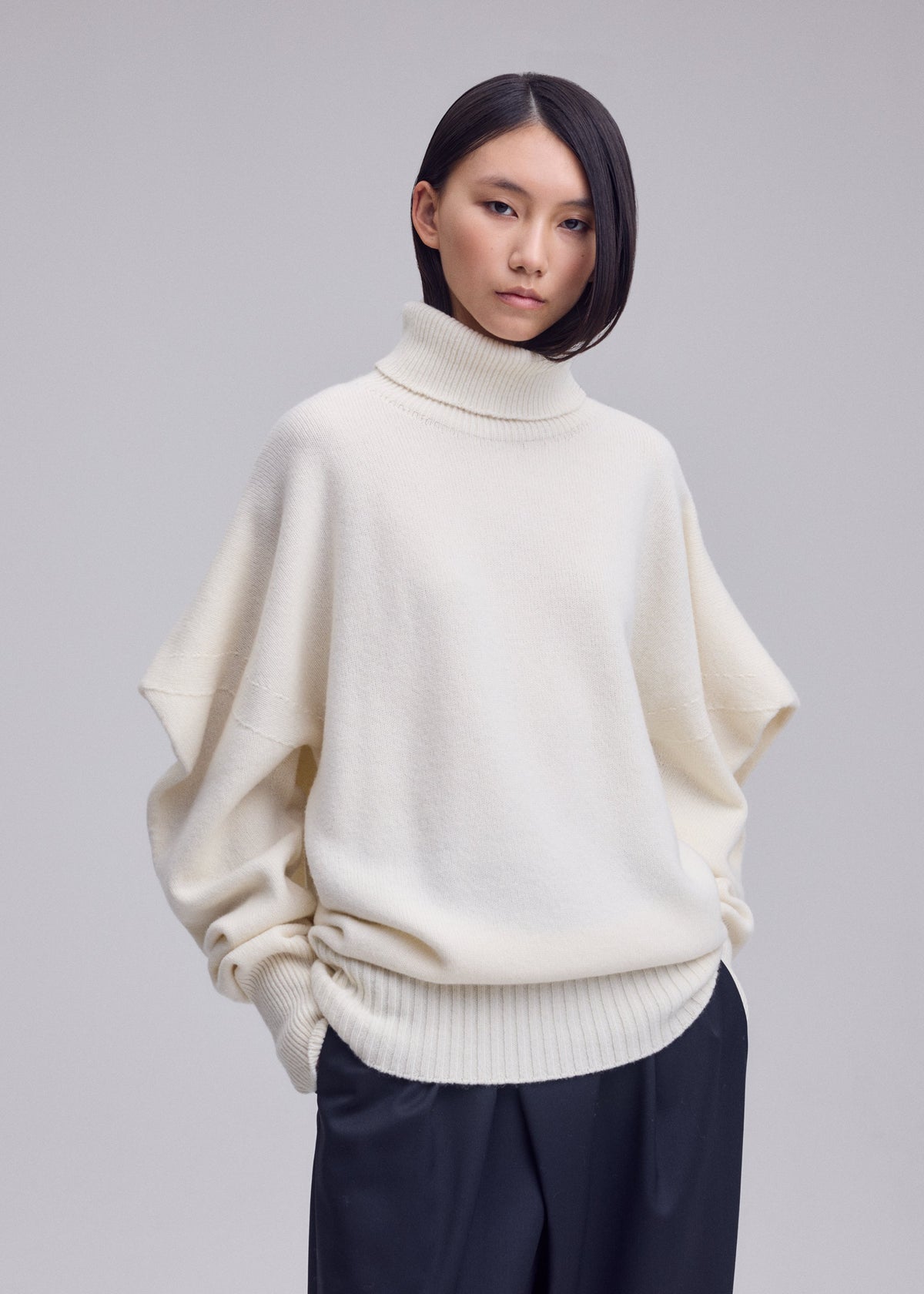 A model wears the ISSEY MIYAKE O KNIT o-knit-high-neck-top-off-white.