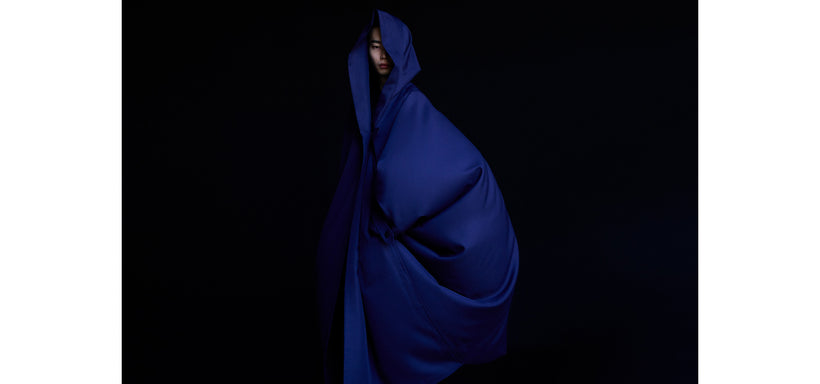 Centre: Model wearing hooded COCOON coat in Navy, posing sideways while looking directly at the camera against a black background.