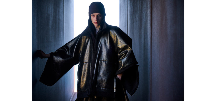 Centre: Model wearing METALLIC ULTRA BOA Jacket Black, looking directly at the camera against grey concrete wall panels, with bright light at the centre.