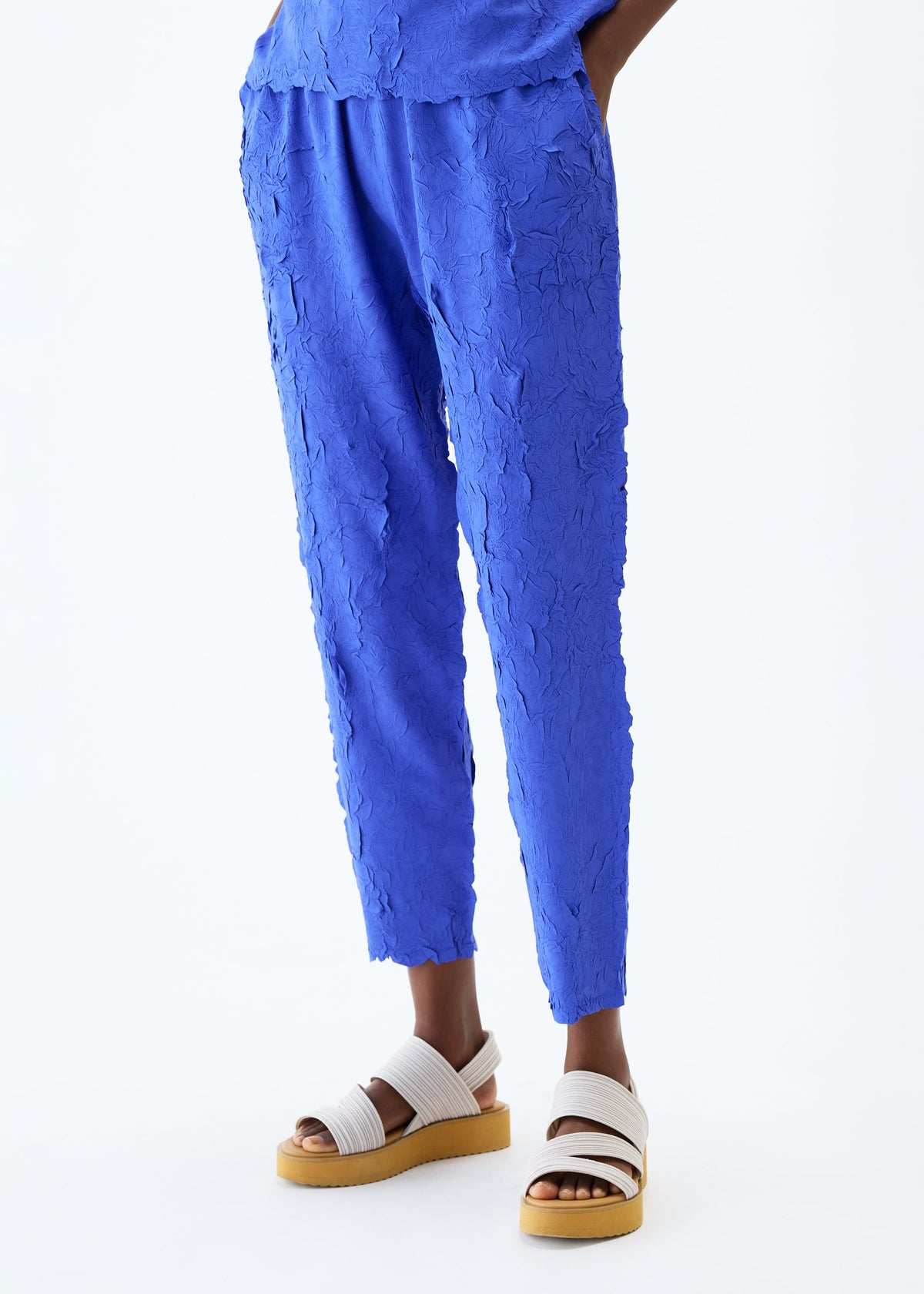 A model wears the PLEATS PLEASE ISSEY MIYAKE CRUSH PRESS trousers.