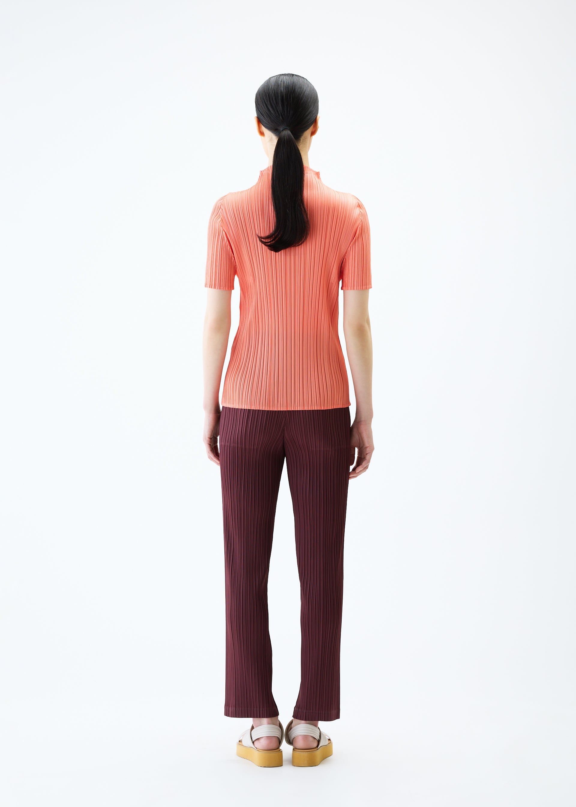 A model wears the PLEATS PLEASE ISSEY MIYAKE LOOP BOTTOMS trousers.