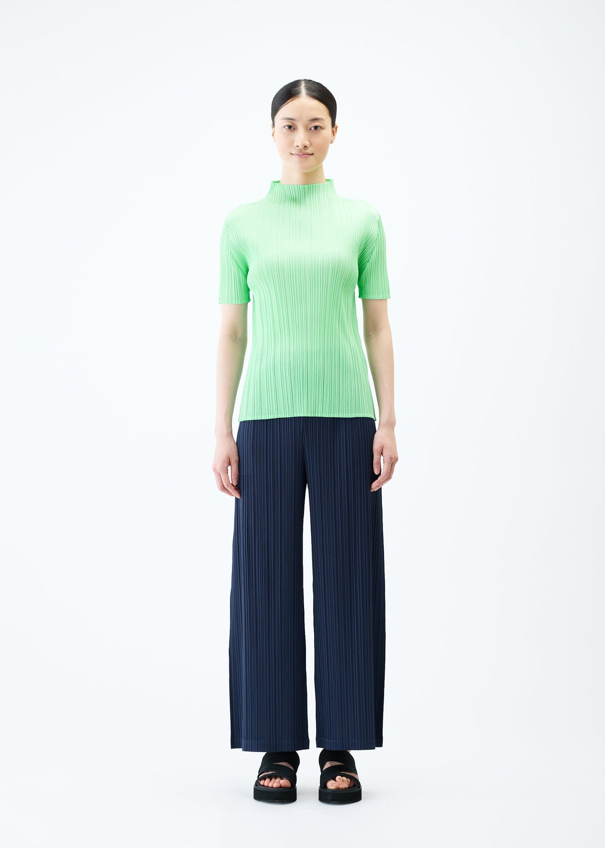 A model wears the PLEATS PLEASE ISSEY MIYAKE LOOP BOTTOMS trousers.