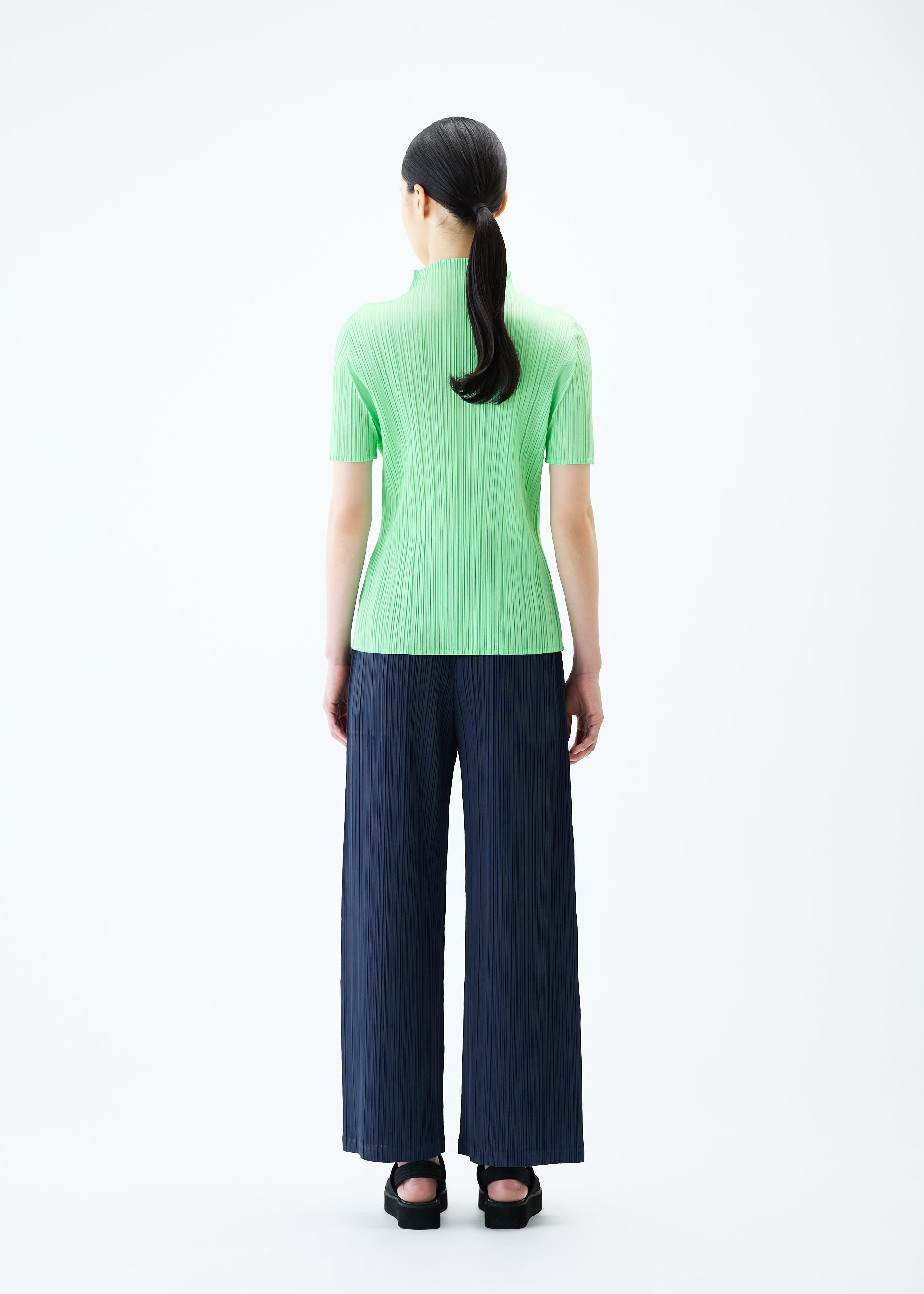 A model wears the PLEATS PLEASE ISSEY MIYAKE LOOP BOTTOMS trousers.
