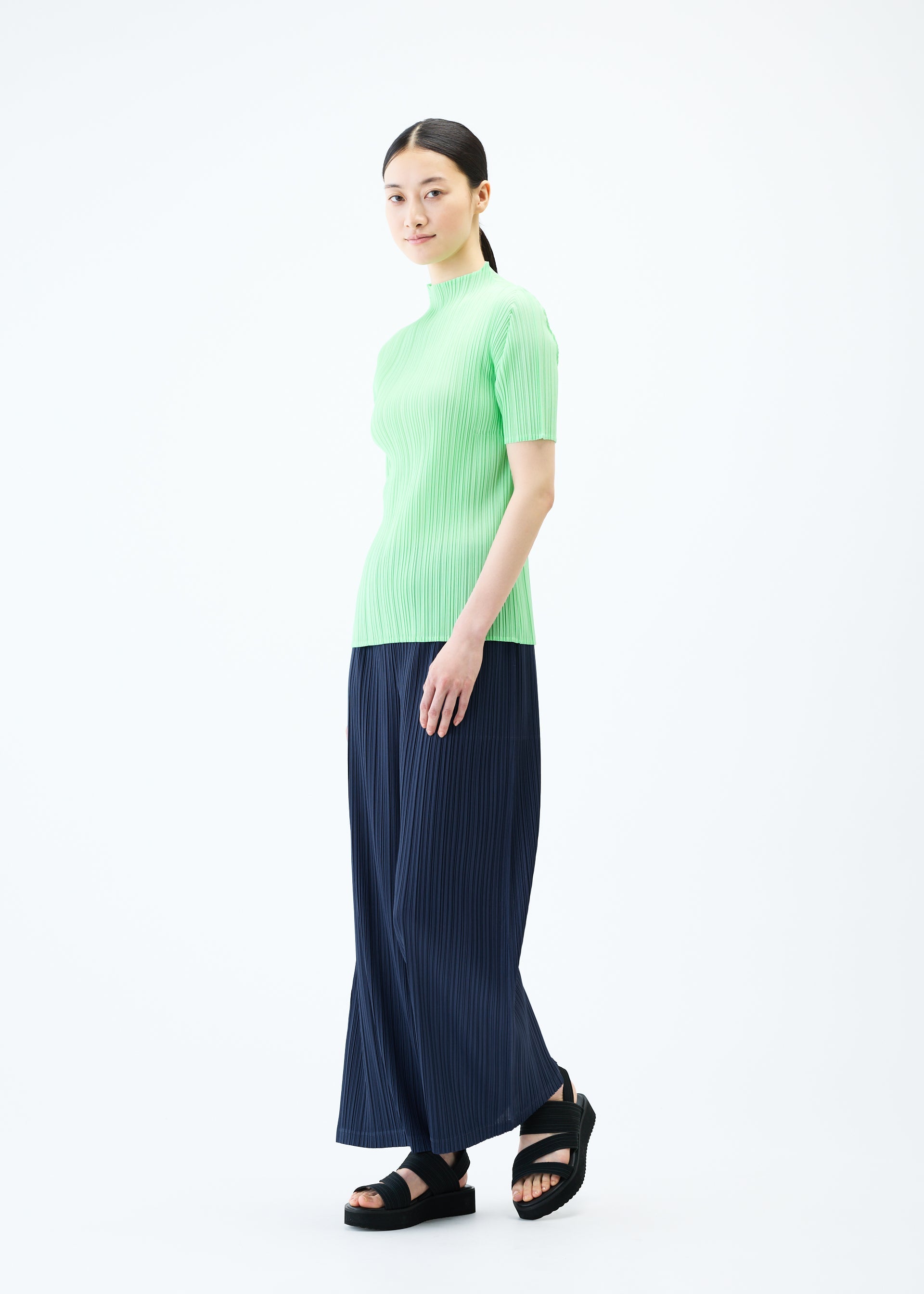 A model wears the PLEATS PLEASE ISSEY MIYAKE LOOP BOTTOMS trousers.