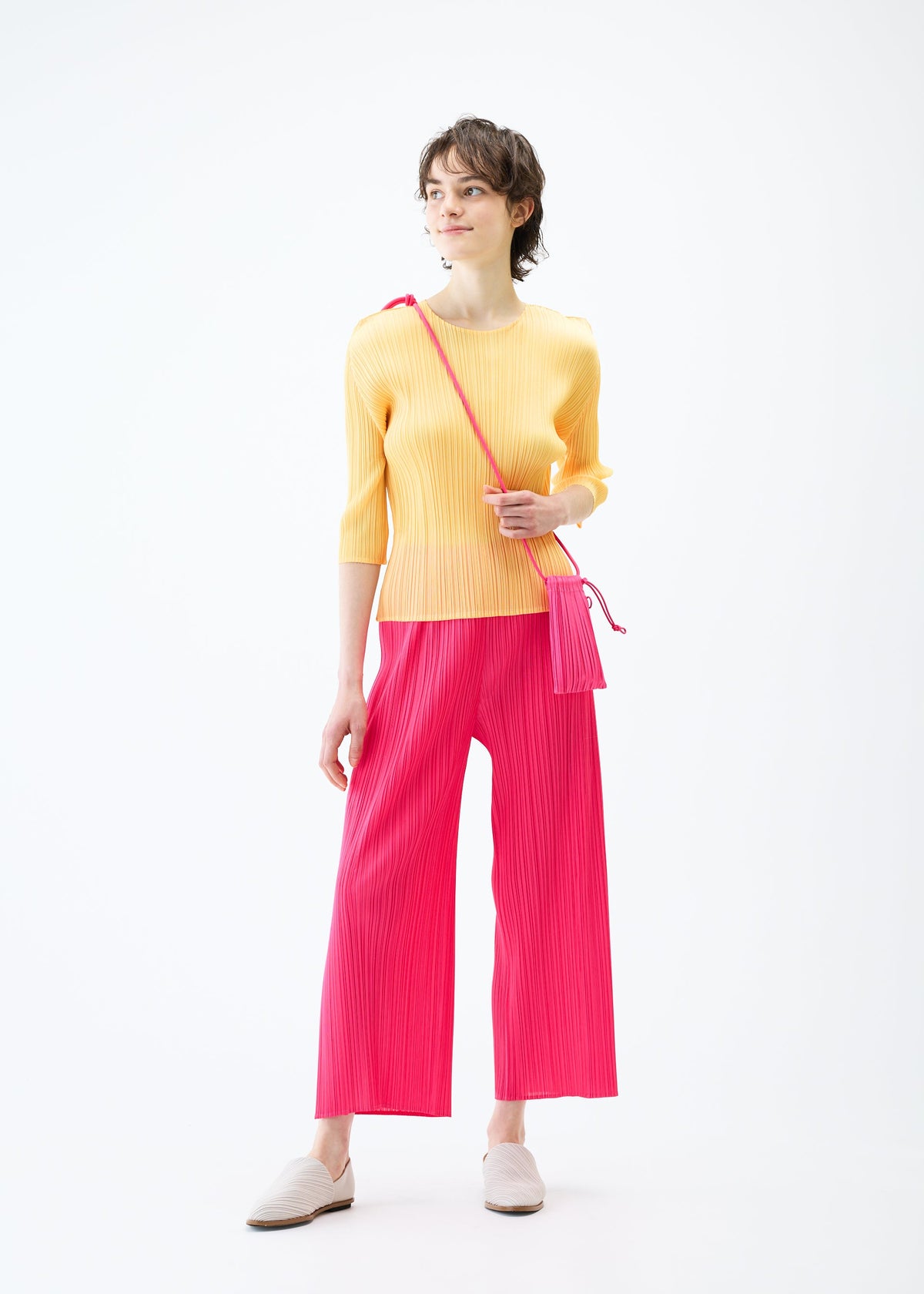 A model wears the PLEATS PLEASE ISSEY MIYAKE PLEATS MINI POCHETTE bag.