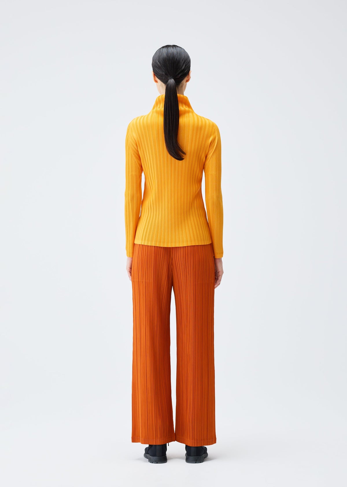 A model wears the PLEATS PLEASE ISSEY MIYAKE LOOP BOTTOMS clothing.