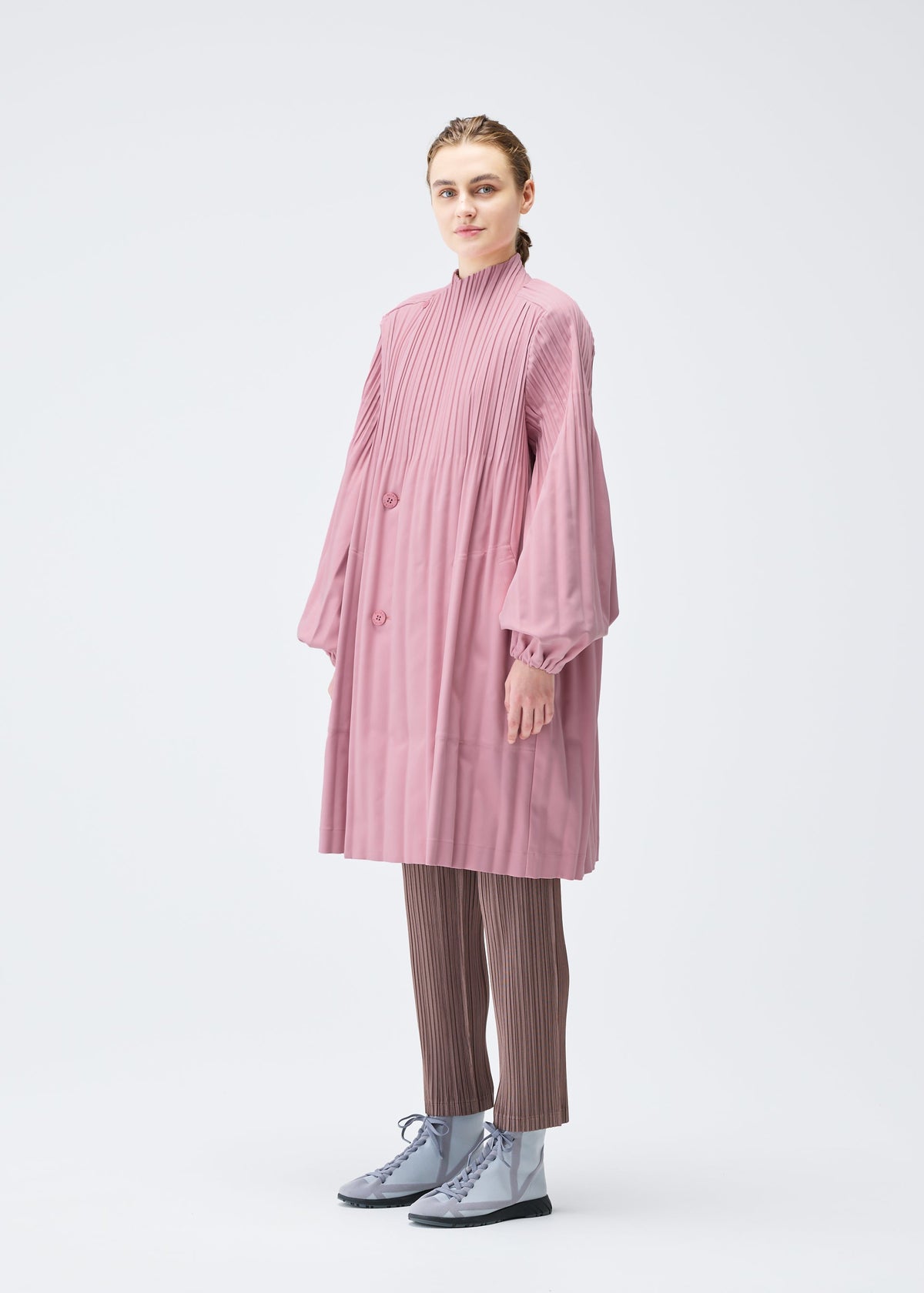 A model wears the PLEATS PLEASE ISSEY MIYAKE SMOOTH COAT coat.