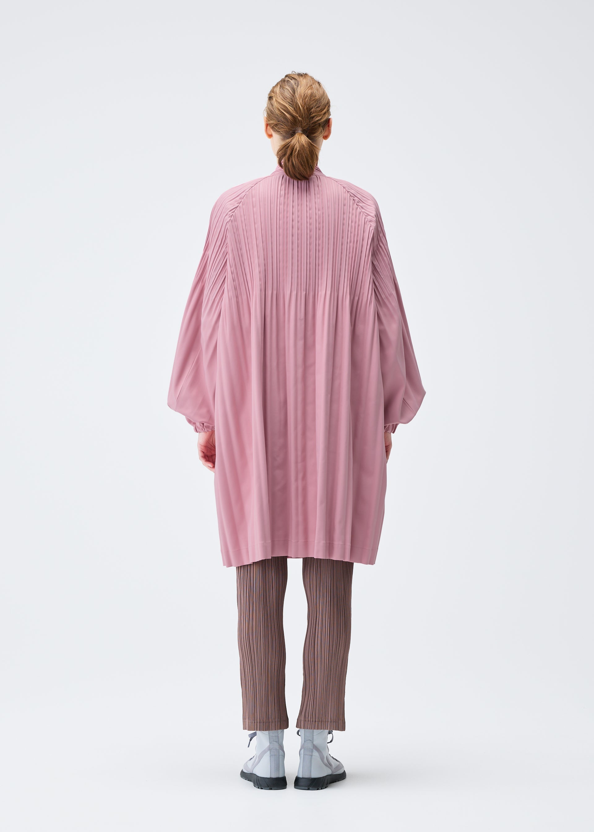 A model wears the PLEATS PLEASE ISSEY MIYAKE SMOOTH COAT coat.