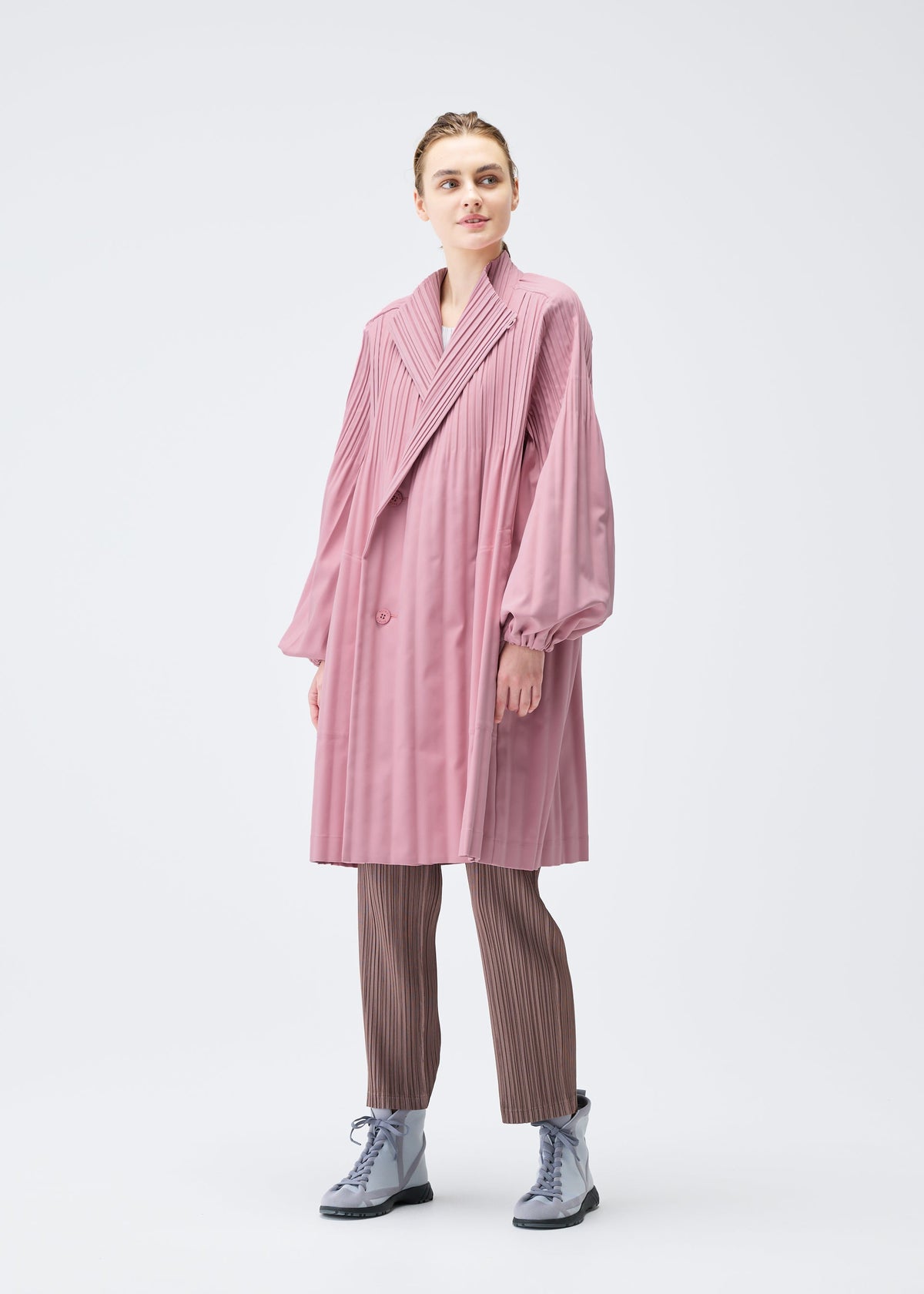 A model wears the PLEATS PLEASE ISSEY MIYAKE SMOOTH COAT coat.