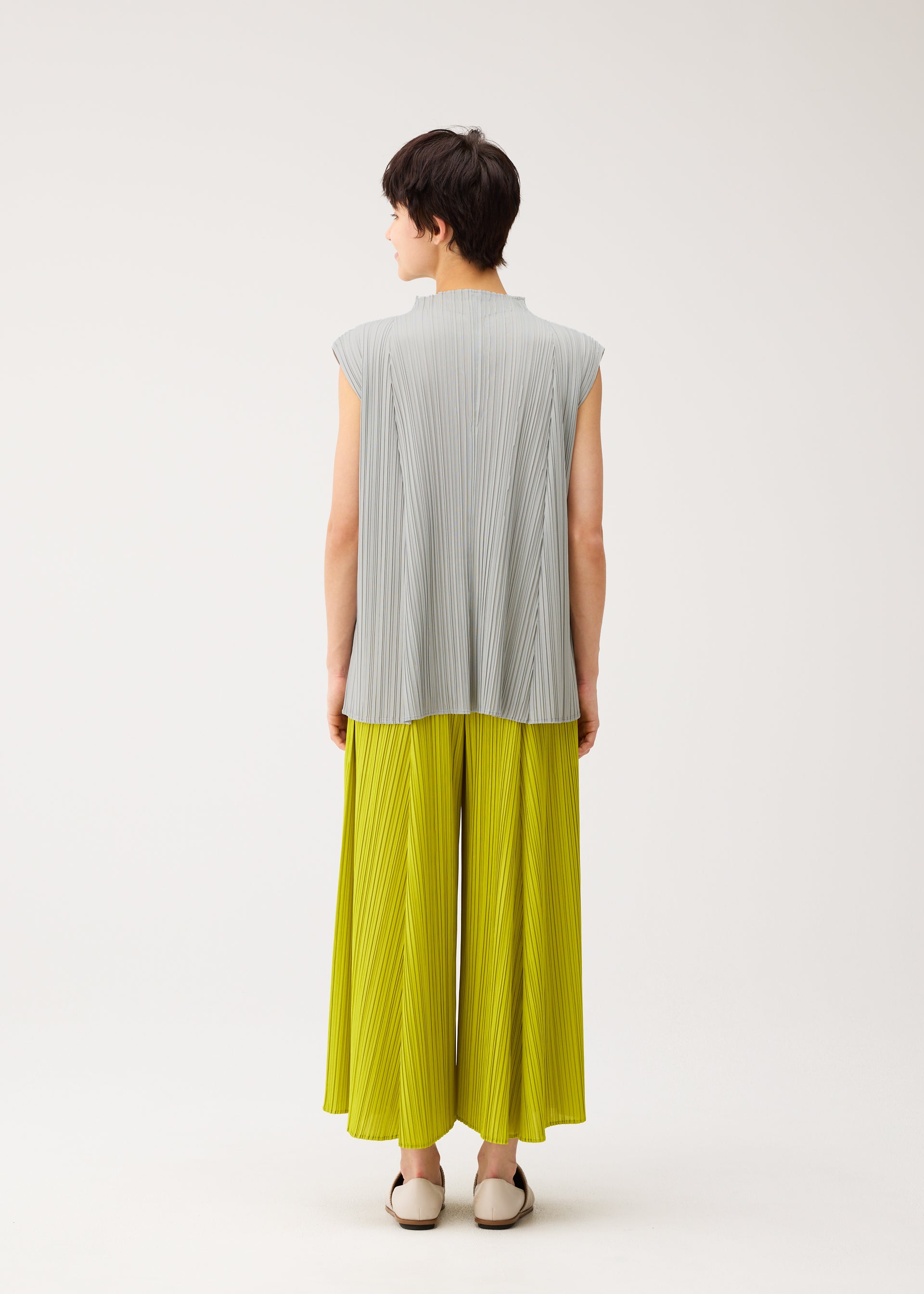 A model wears the PLEATS PLEASE ISSEY MIYAKE MELLOW PLEATS trousers.