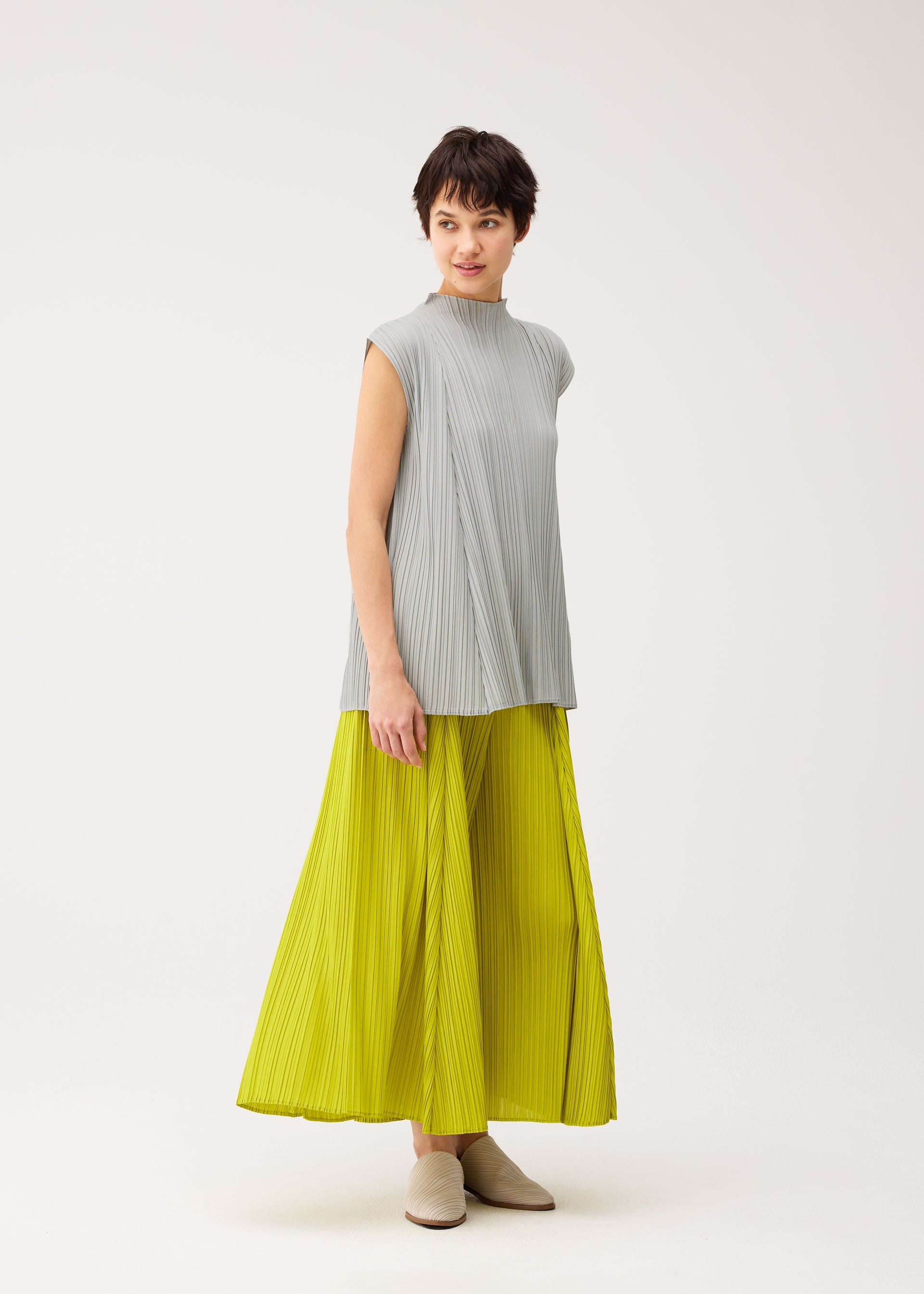 A model wears the PLEATS PLEASE ISSEY MIYAKE MELLOW PLEATS trousers.