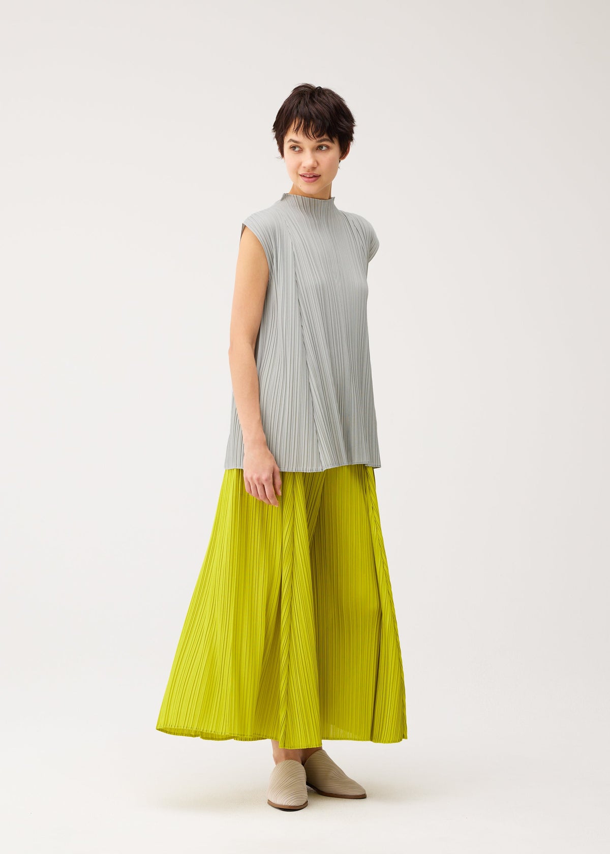 A model wears the PLEATS PLEASE ISSEY MIYAKE MELLOW PLEATS trousers.