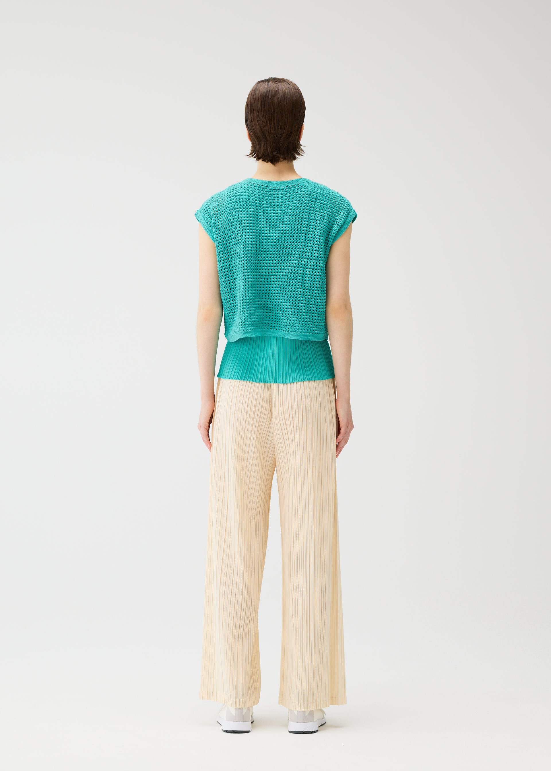 A model wears the PLEATS PLEASE ISSEY MIYAKE LOOP BOTTOMS trousers.