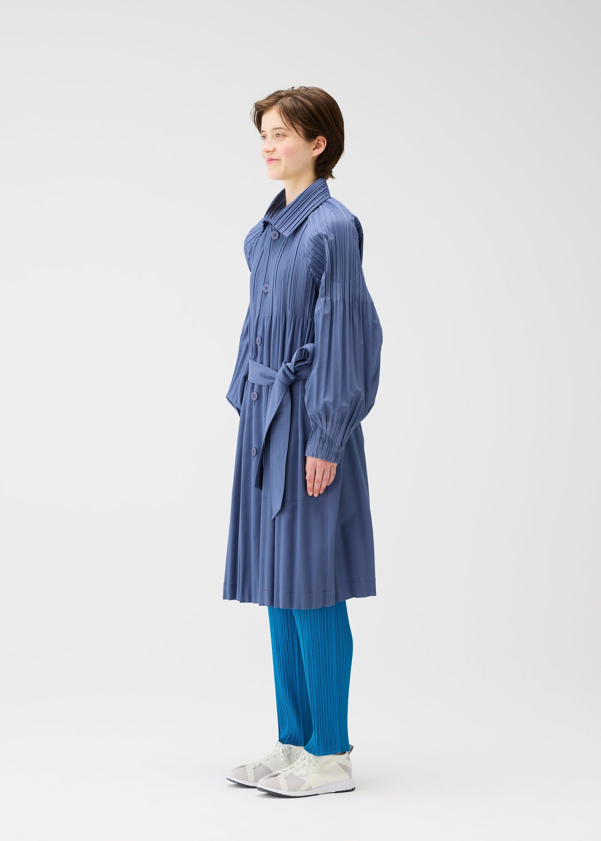 A model wears the PLEATS PLEASE ISSEY MIYAKE SMOOTH COAT coat.