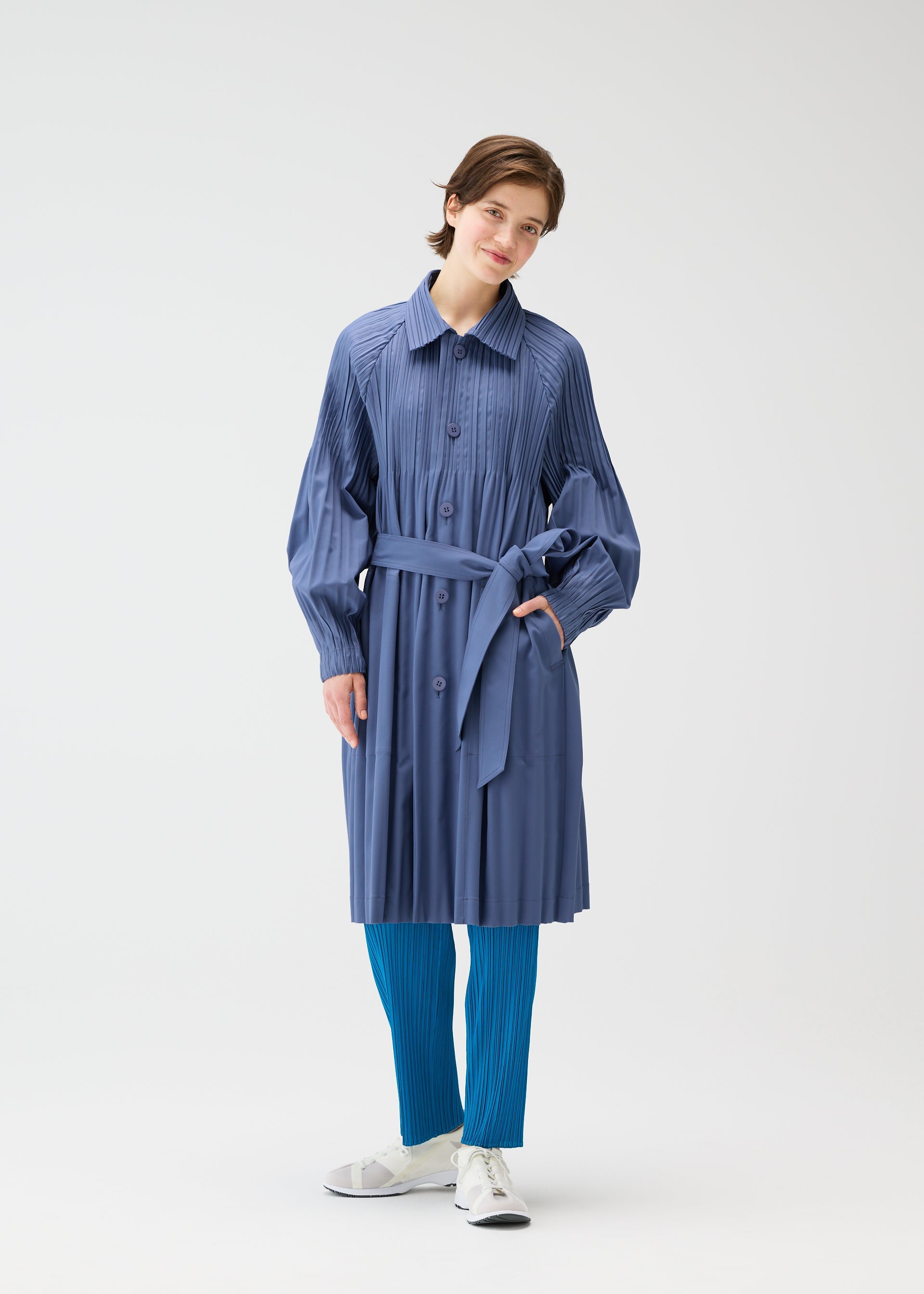 A model wears the PLEATS PLEASE ISSEY MIYAKE SMOOTH COAT coat.