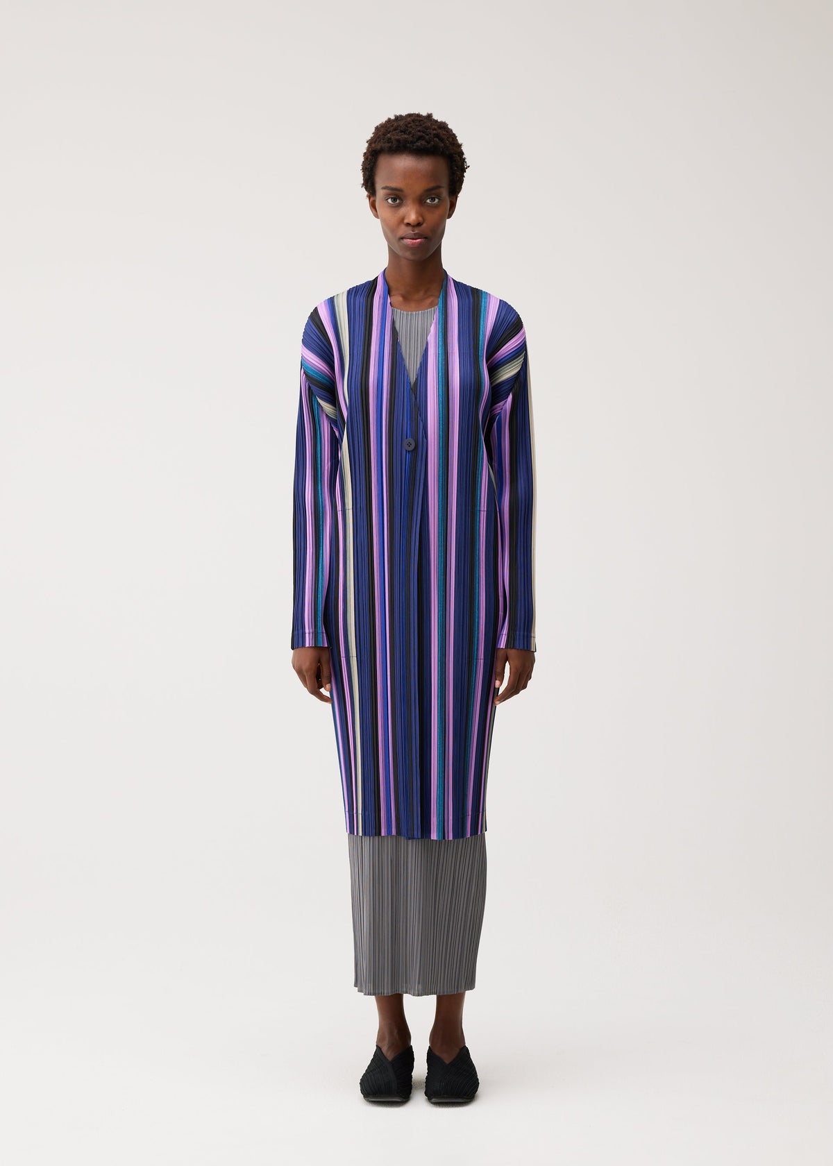 A model wears the PLEATS PLEASE ISSEY MIYAKE TAPE TAPE tape-tape-coat-purple.