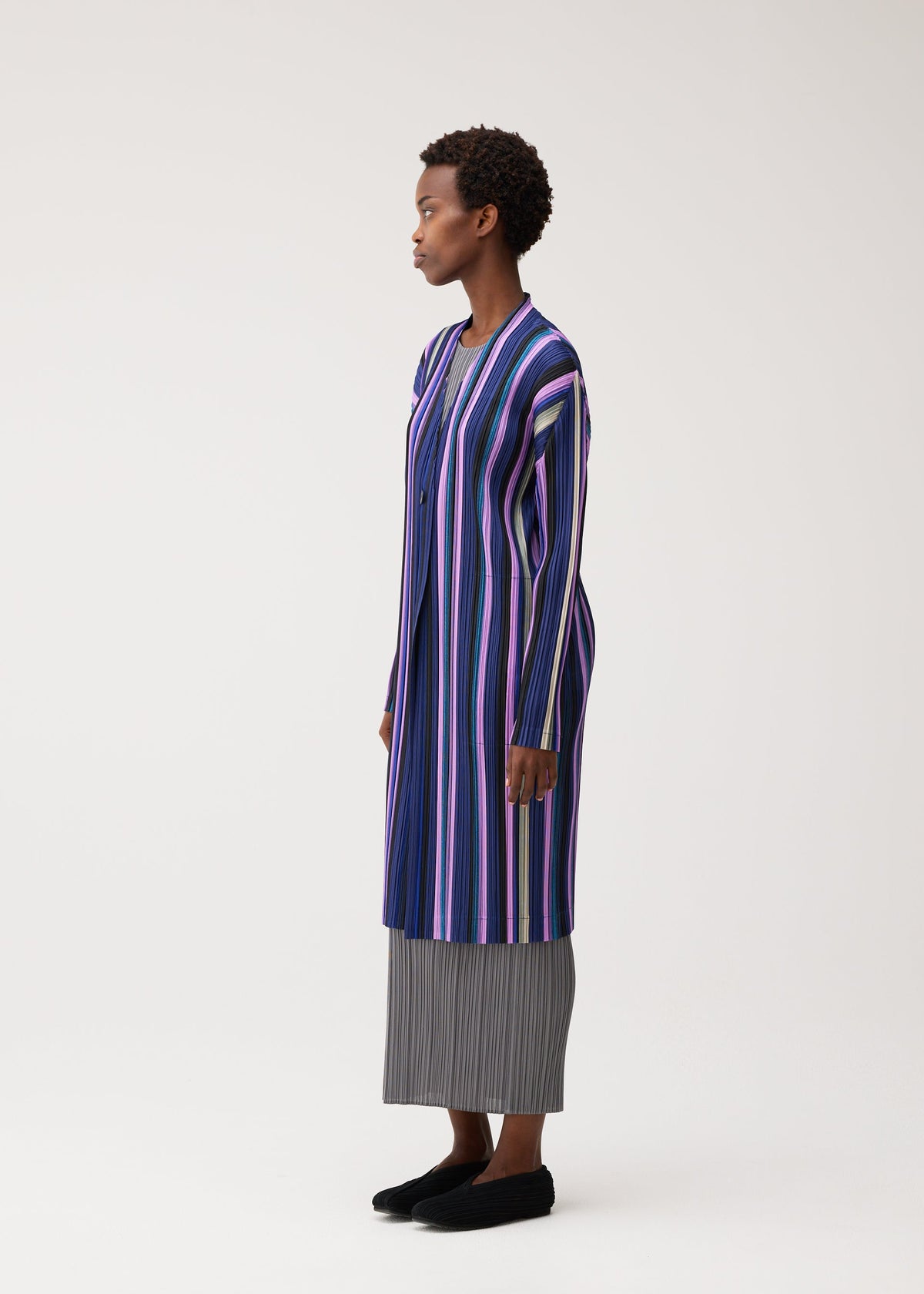 A model wears the PLEATS PLEASE ISSEY MIYAKE TAPE TAPE tape-tape-coat-purple.